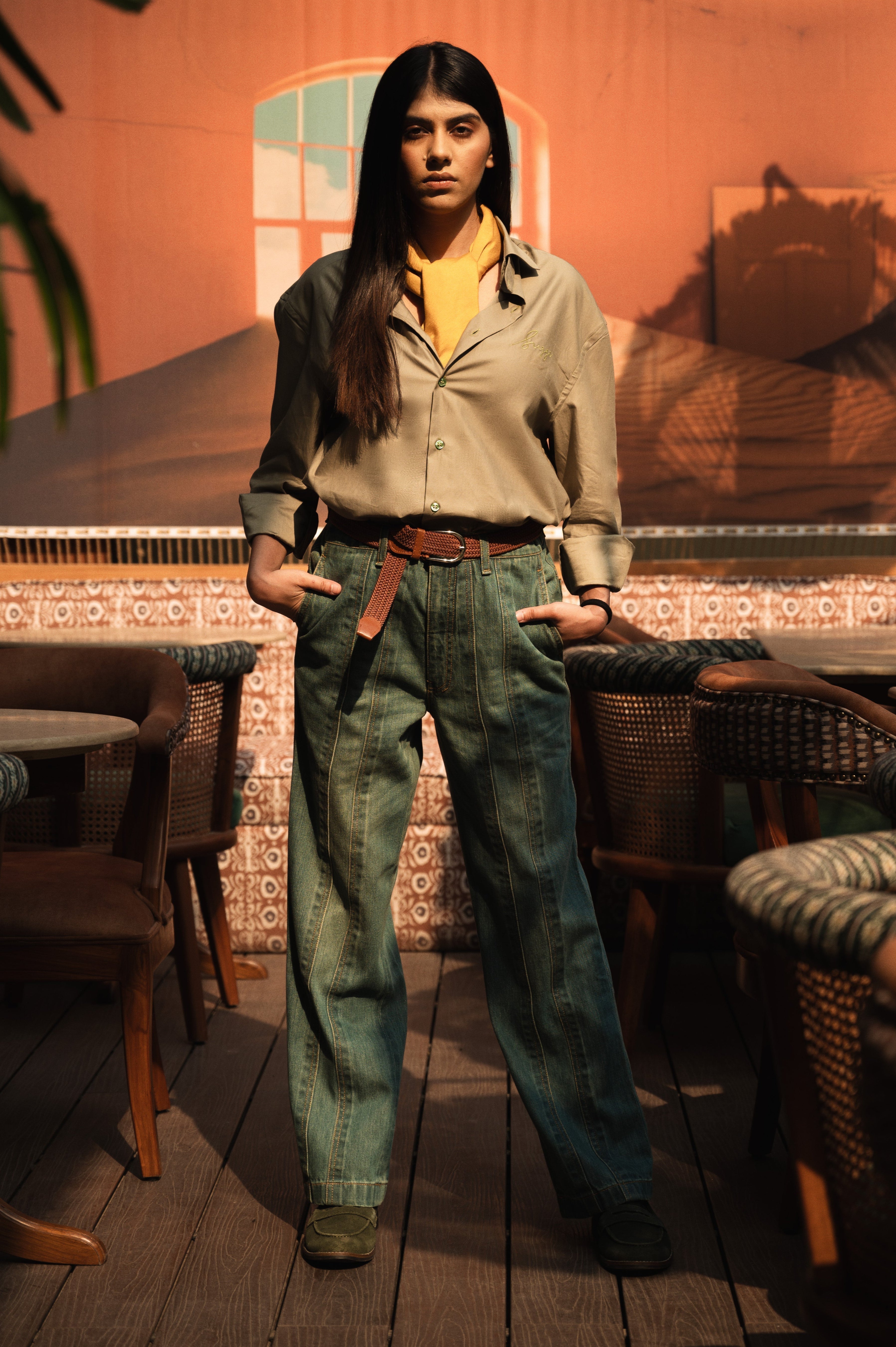 Woman in casual streetwear, beige shirt and green wide-leg jeans, standing indoors