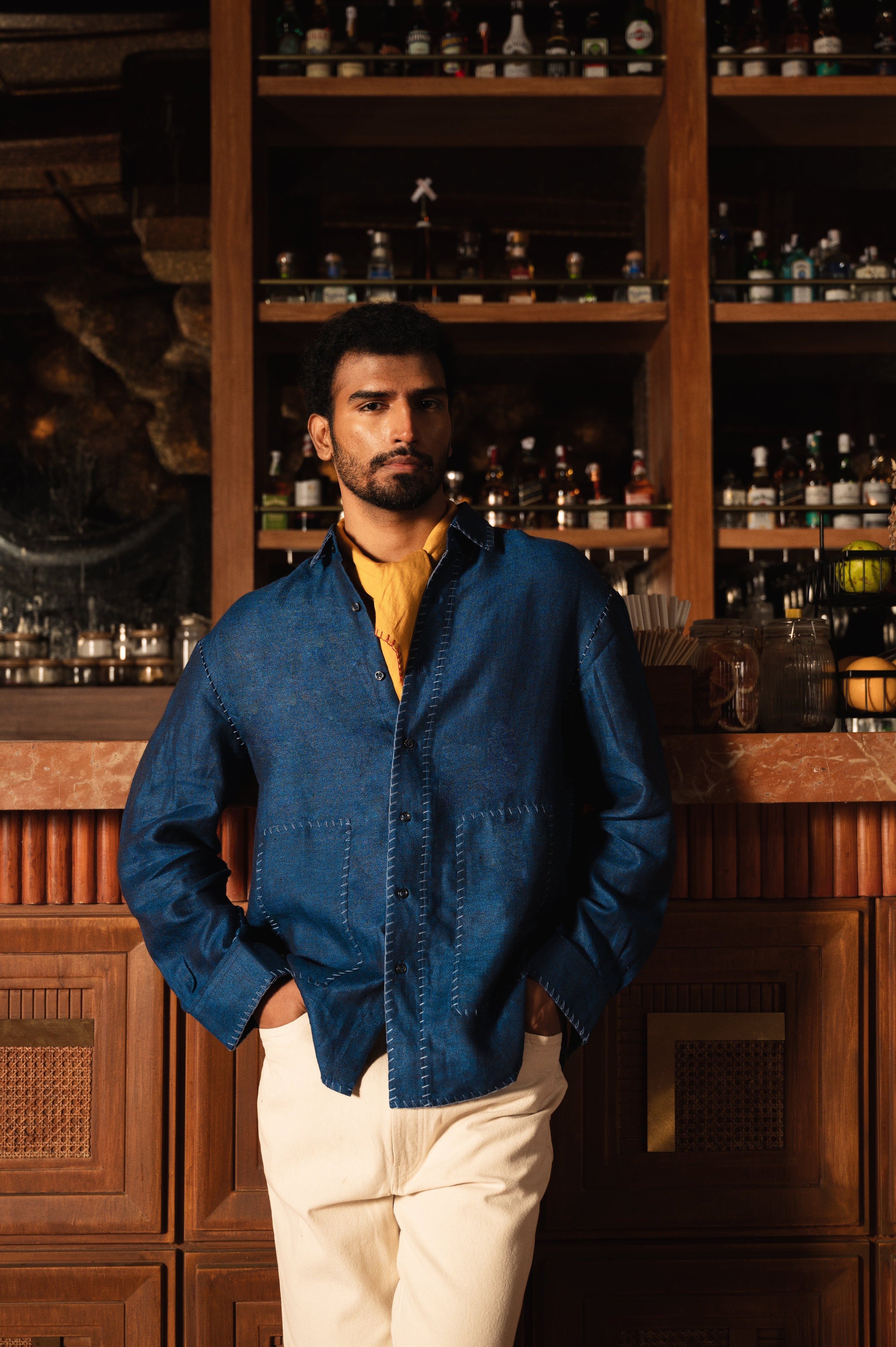 Man in blue denim overshirt and cream pants posing indoors, stylish streetwear fashion