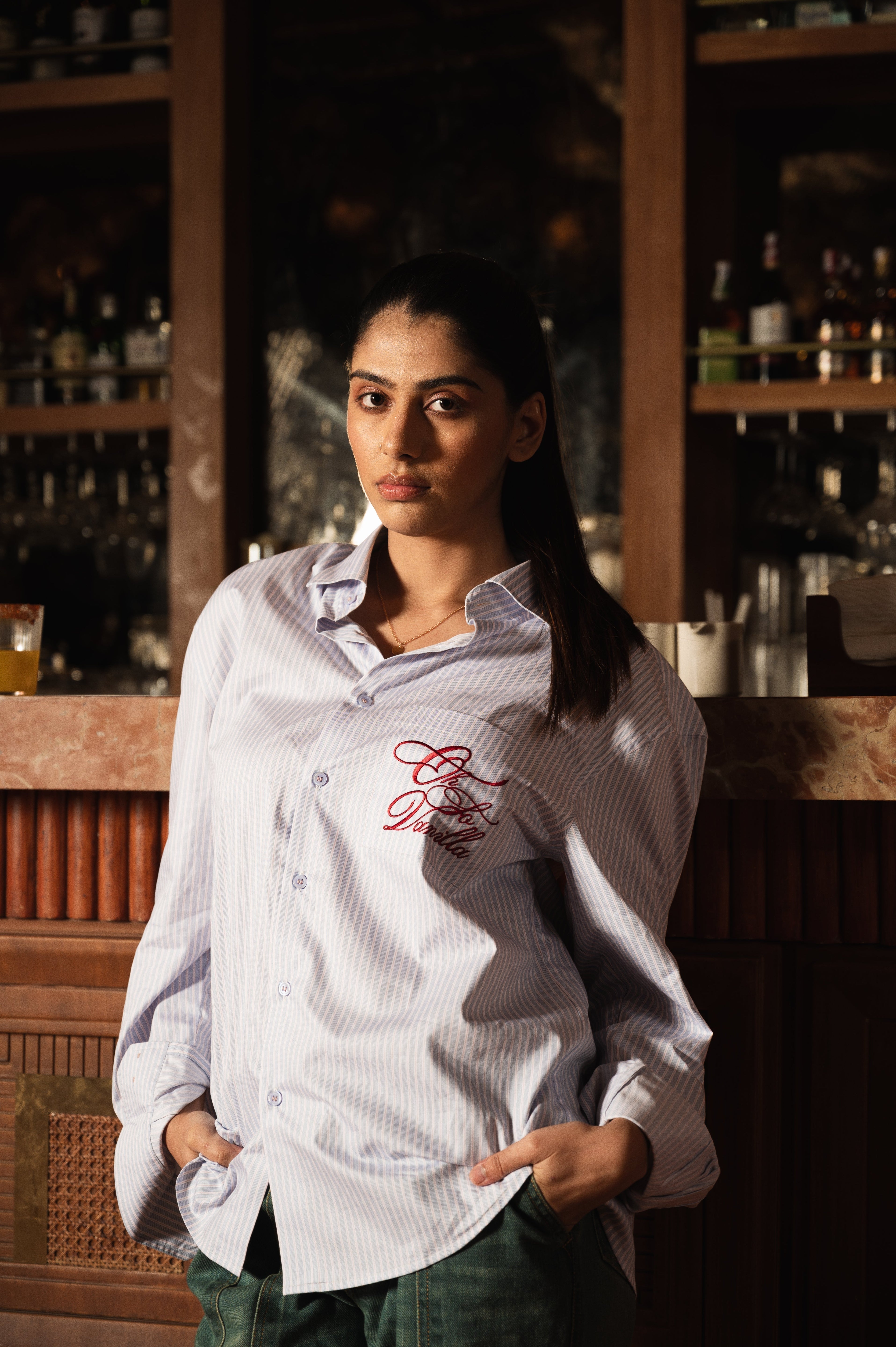 Woman wearing oversized striped button-up shirt with red embroidery, styled streetwear fashion.