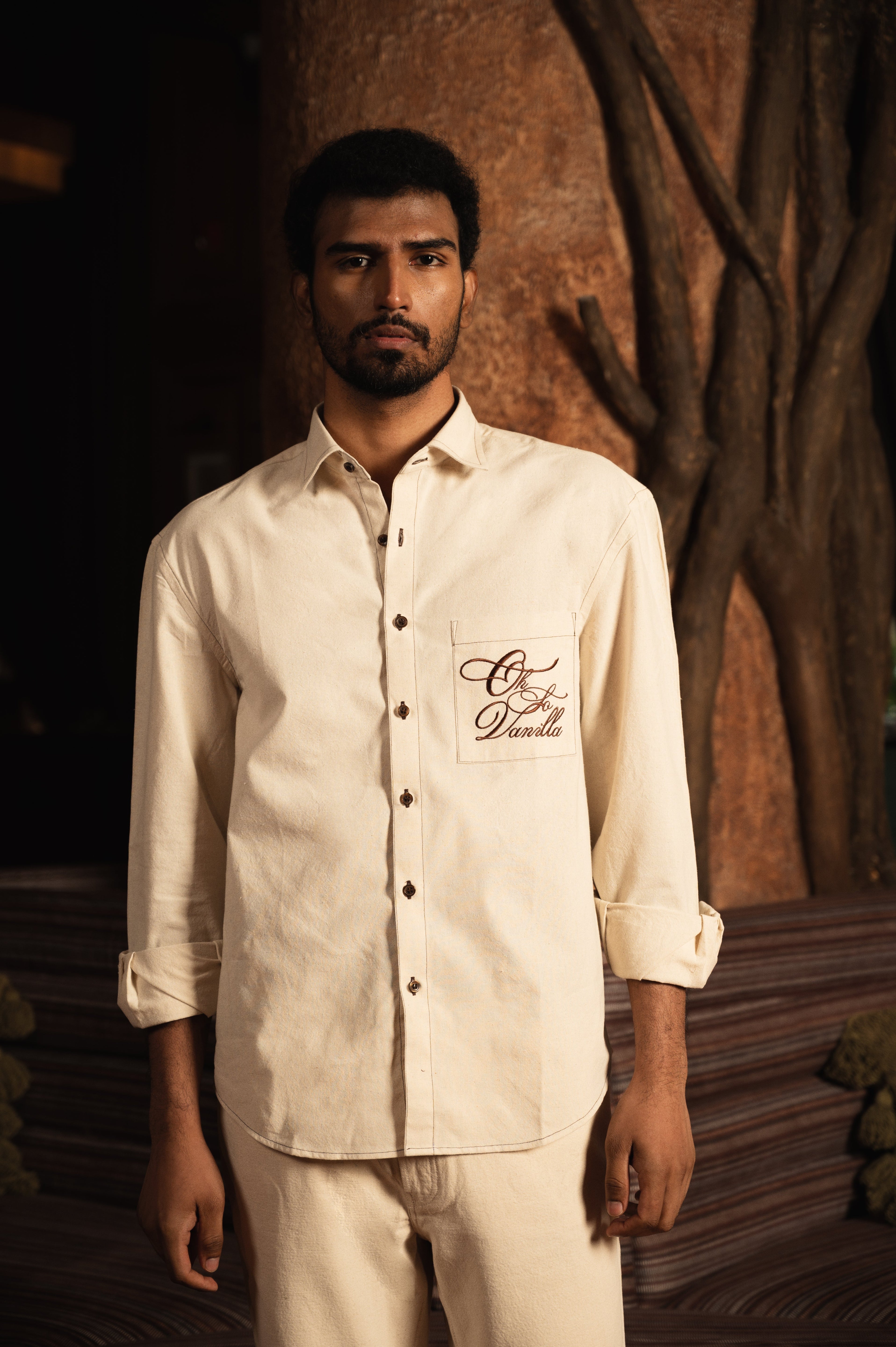Man wearing a cream long sleeve streetwear shirt with pocket embroidery, neutral background