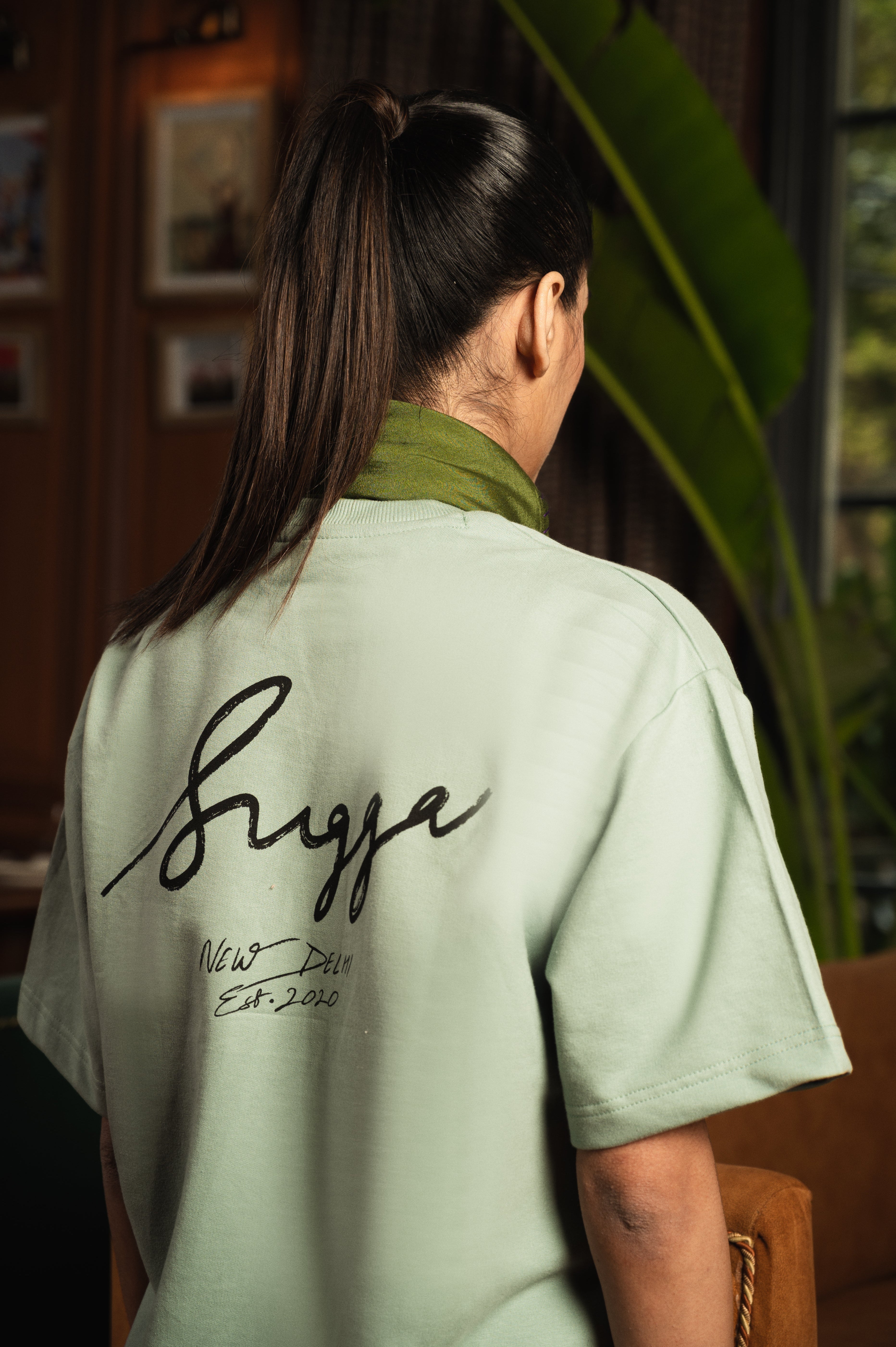 Woman in ponytail wearing light green streetwear t-shirt with Sugga New Delhi Est.2020 text