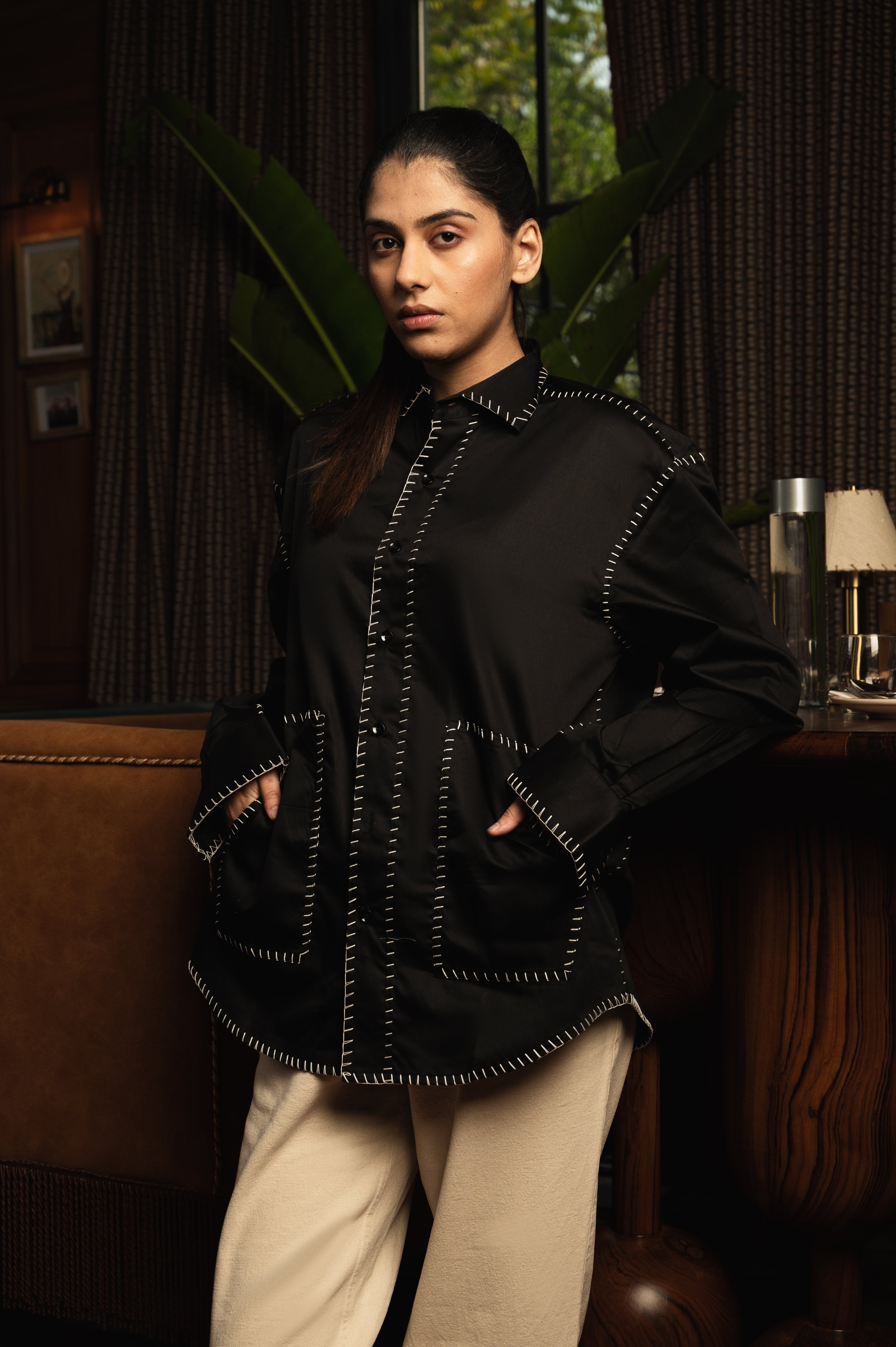 Woman in a black oversized streetwear jacket with white contrast stitching and beige pants indoors