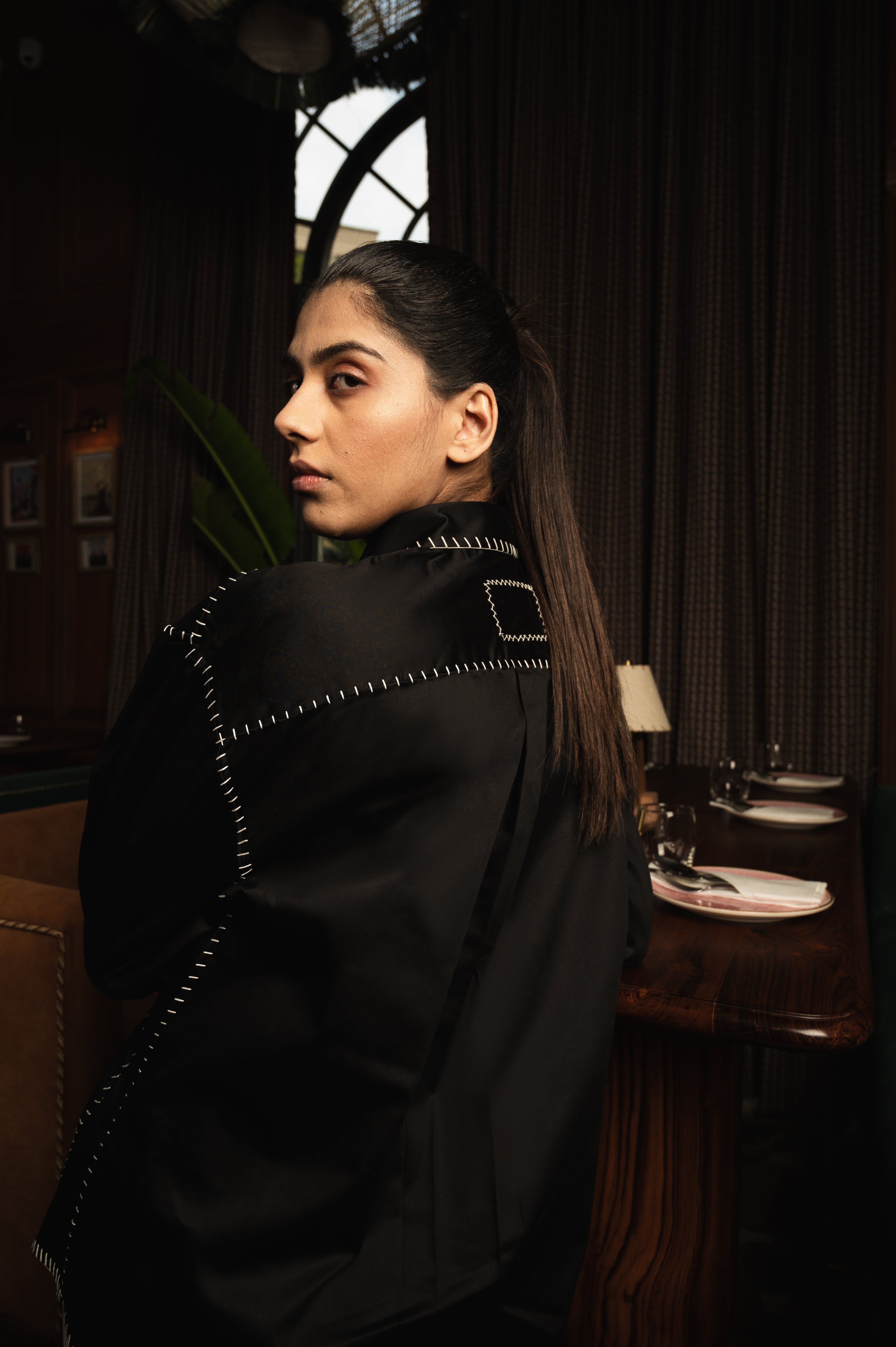 Woman in black streetwear jacket with white stitching, standing indoors, luxury fashion