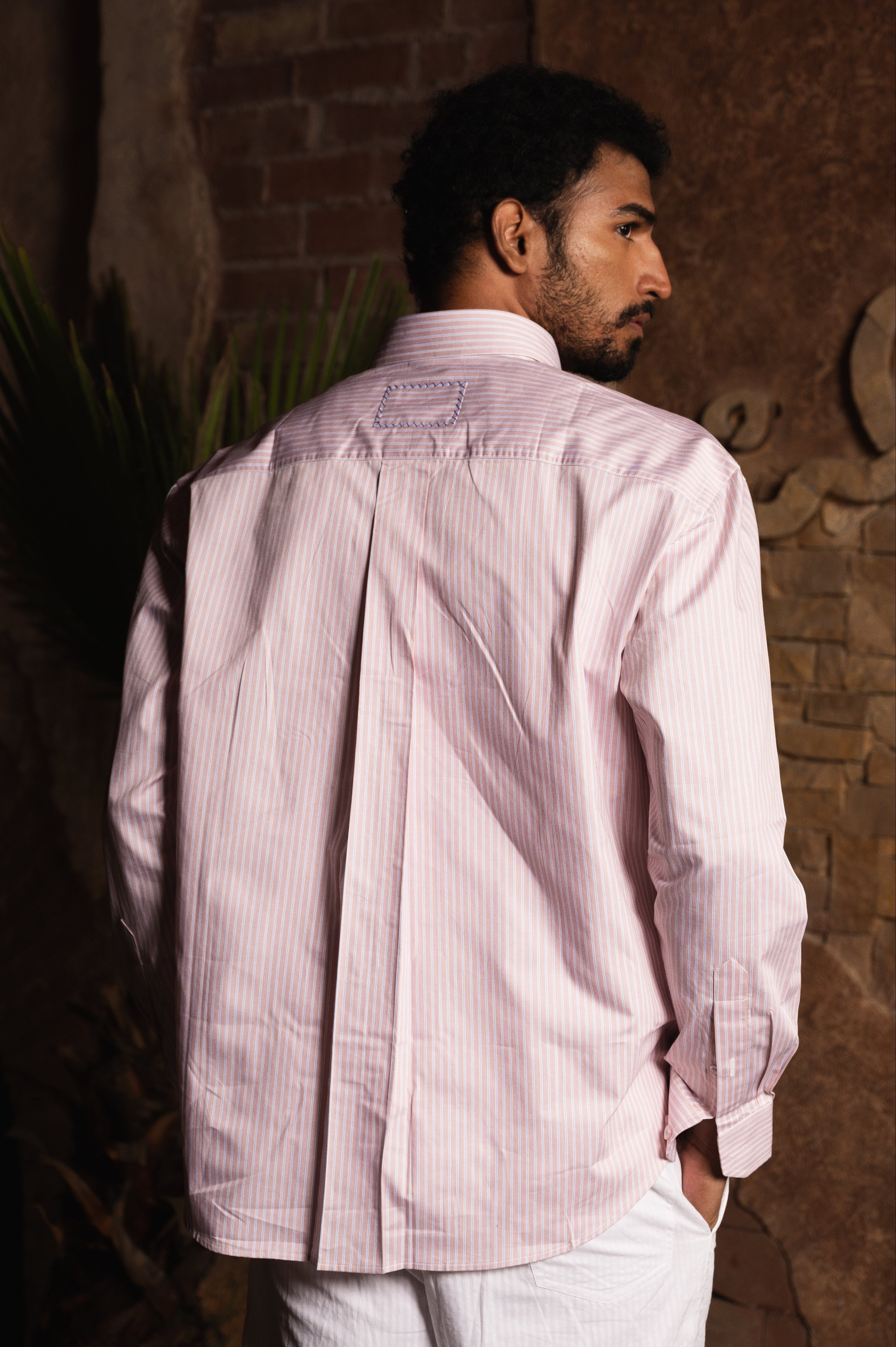 Man wearing pastel pink striped long-sleeve dress shirt and white pants, back view