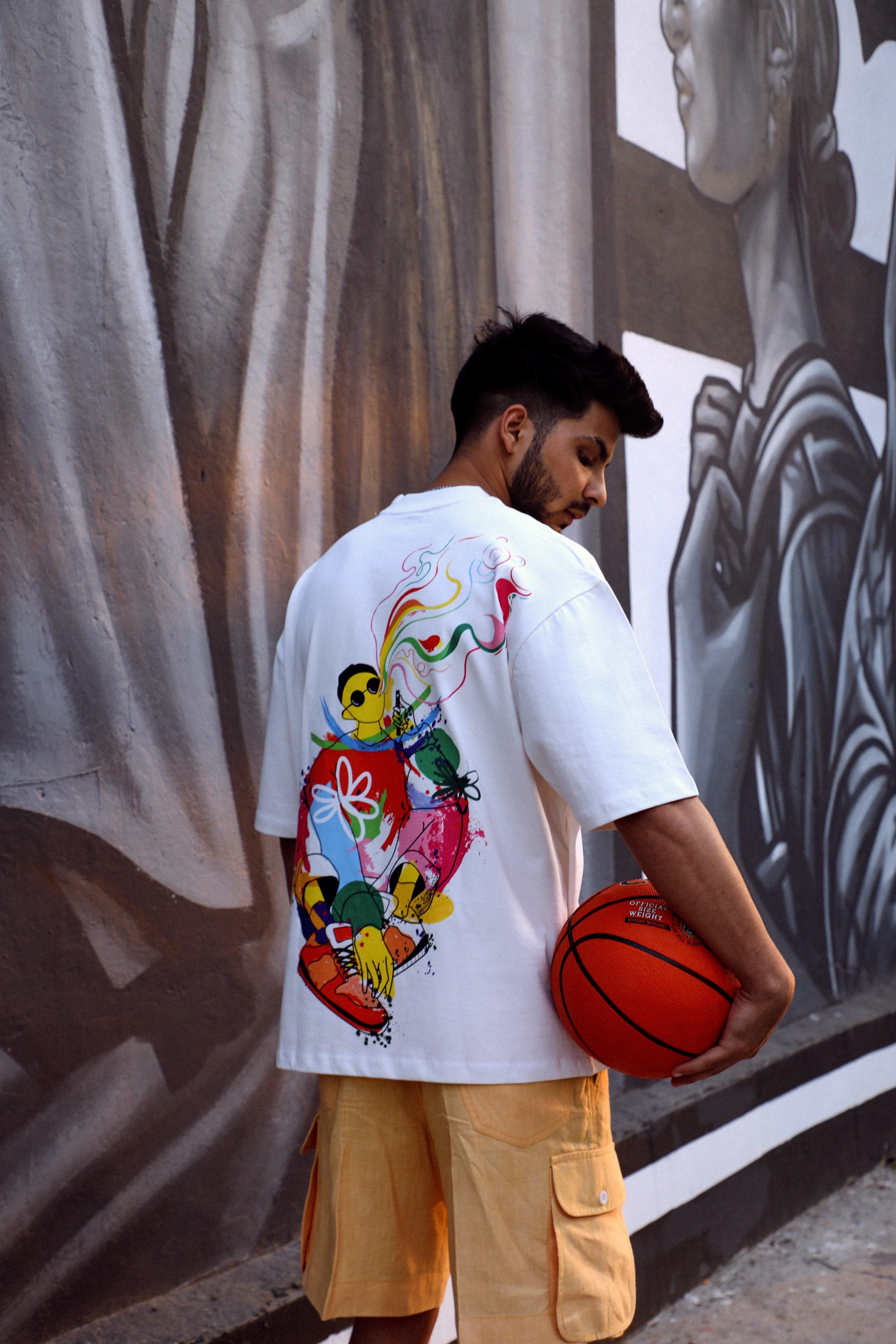 Man in graphic streetwear t-shirt and cargo shorts holding basketball, urban mural background