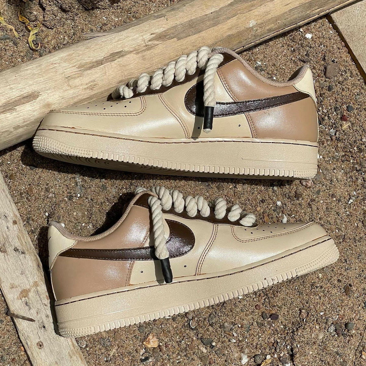 Beige and brown low-top sneakers with thick rope laces on sandy ground