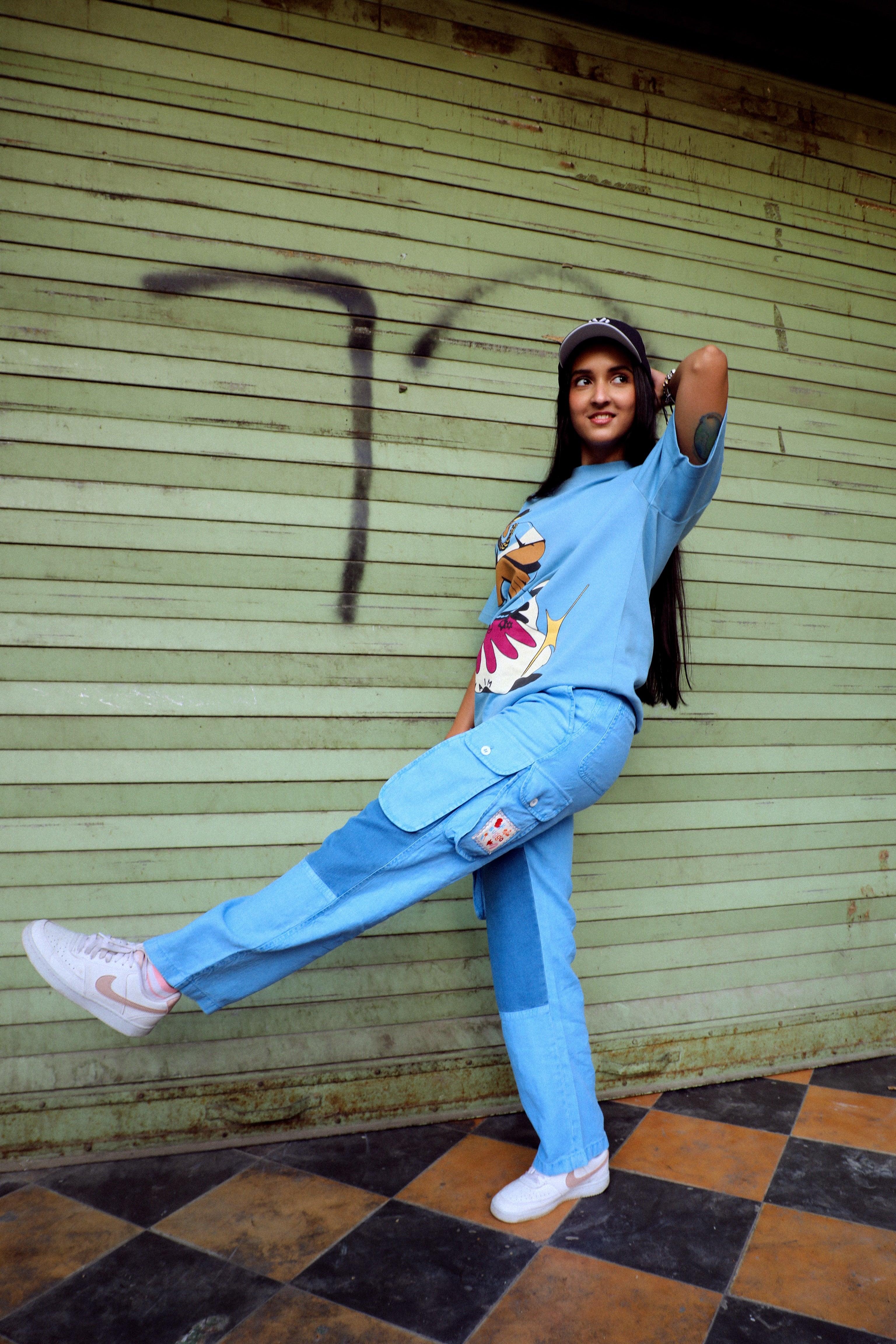 Woman in blue streetwear cargo pants, graphic tee, and sneakers posing by graffiti wall