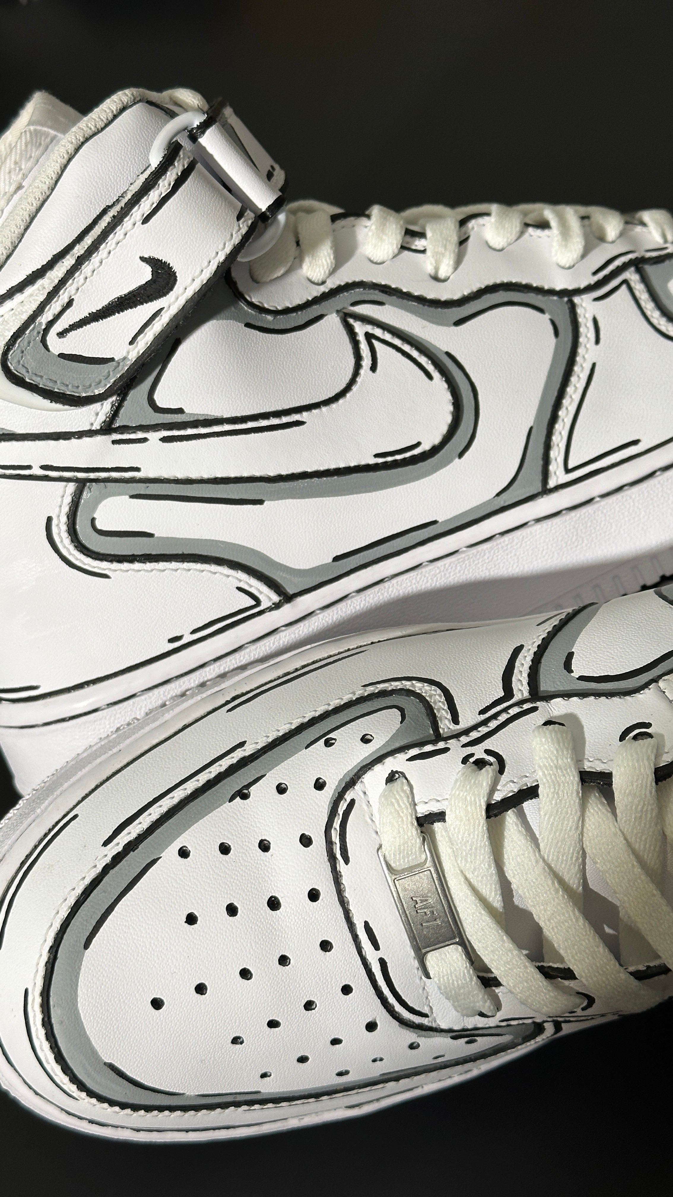 Close-up of white high-top streetwear sneakers with black sketch-style outlines and perforated toe