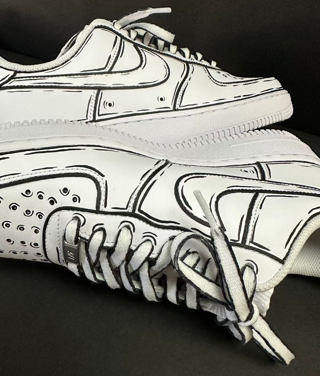 White streetwear sneakers with cartoon-style black outline details on a black background