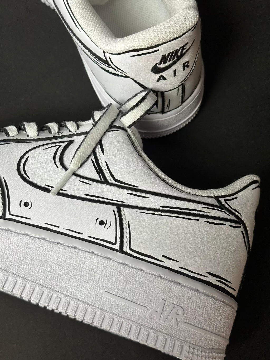 White Nike Air Force 1 sneakers with black cartoon-style outline detailing on a black background