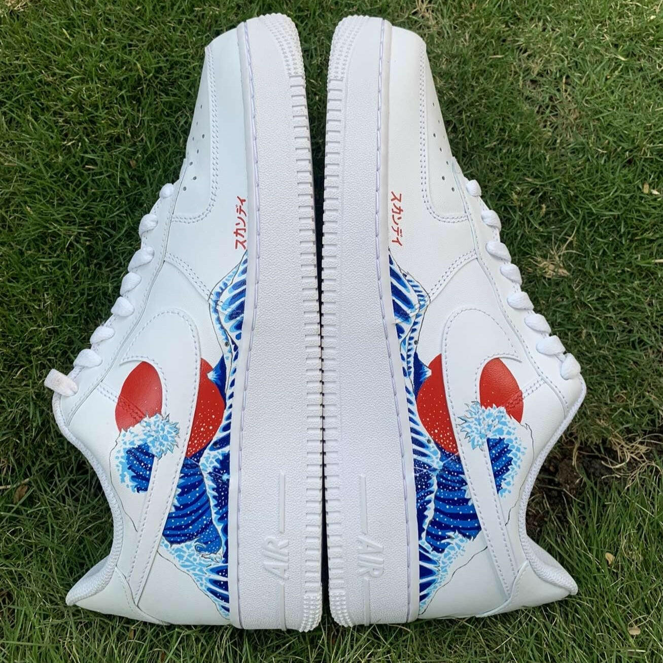 White streetwear sneakers with blue wave and red sun graphic design, displayed on grass
