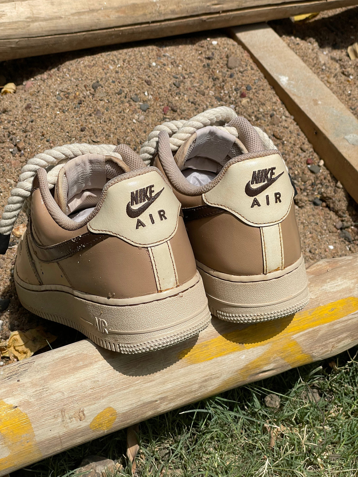 Beige Nike Air sneakers with cream accents placed outdoors on sand and wooden planks