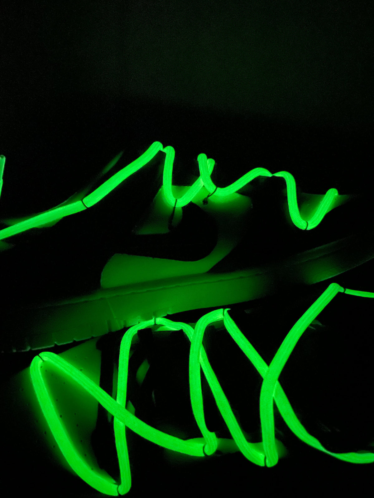 Black sneaker with neon green glow-in-the-dark laces in a dark setting