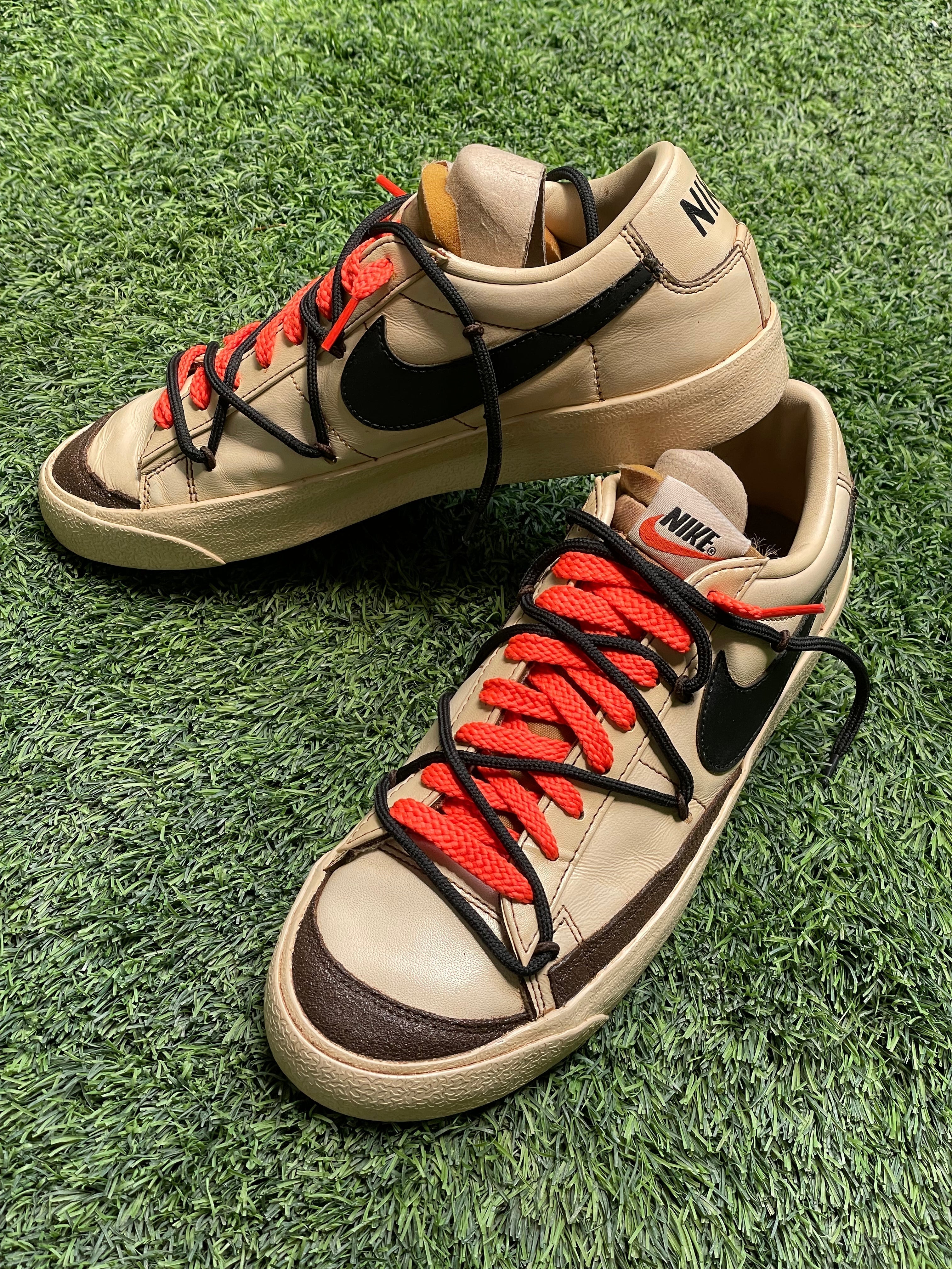 Tan Nike low-top sneakers with black and red laces on green grass, streetwear style