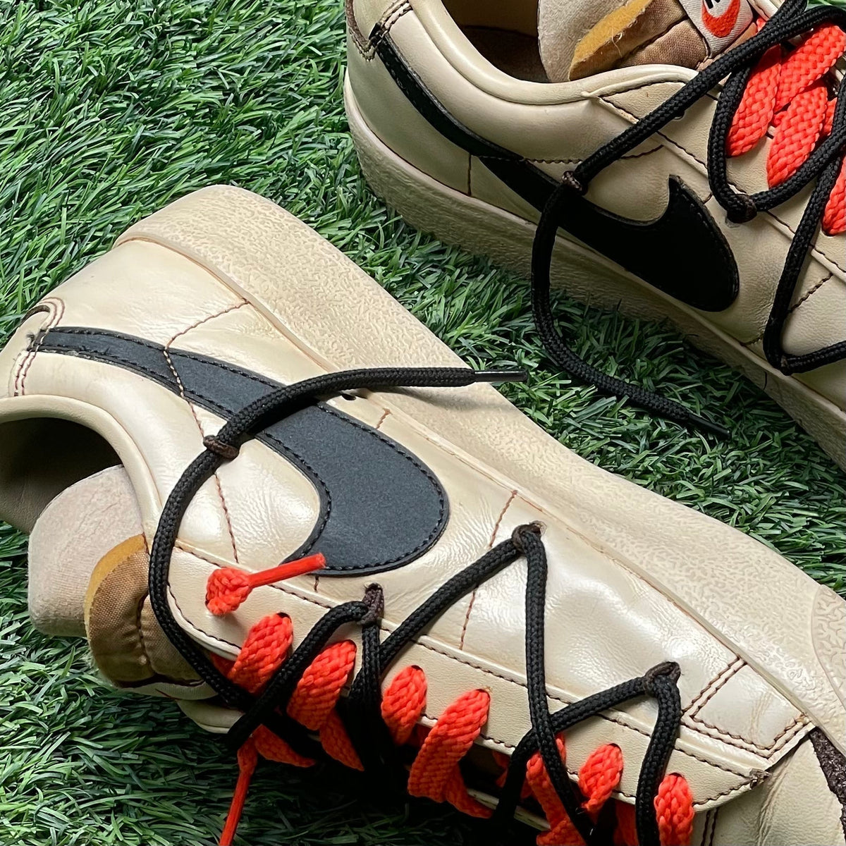 Beige and black designer sneakers with bold red and black laces on green grass