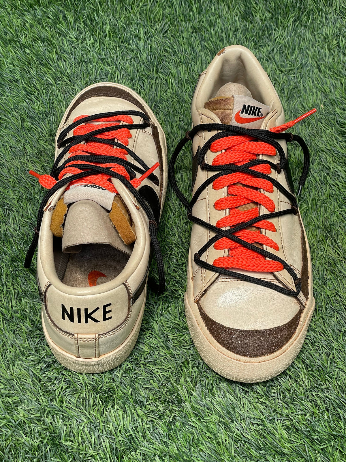 Beige Nike low-top sneakers with red and black laces on green artificial grass