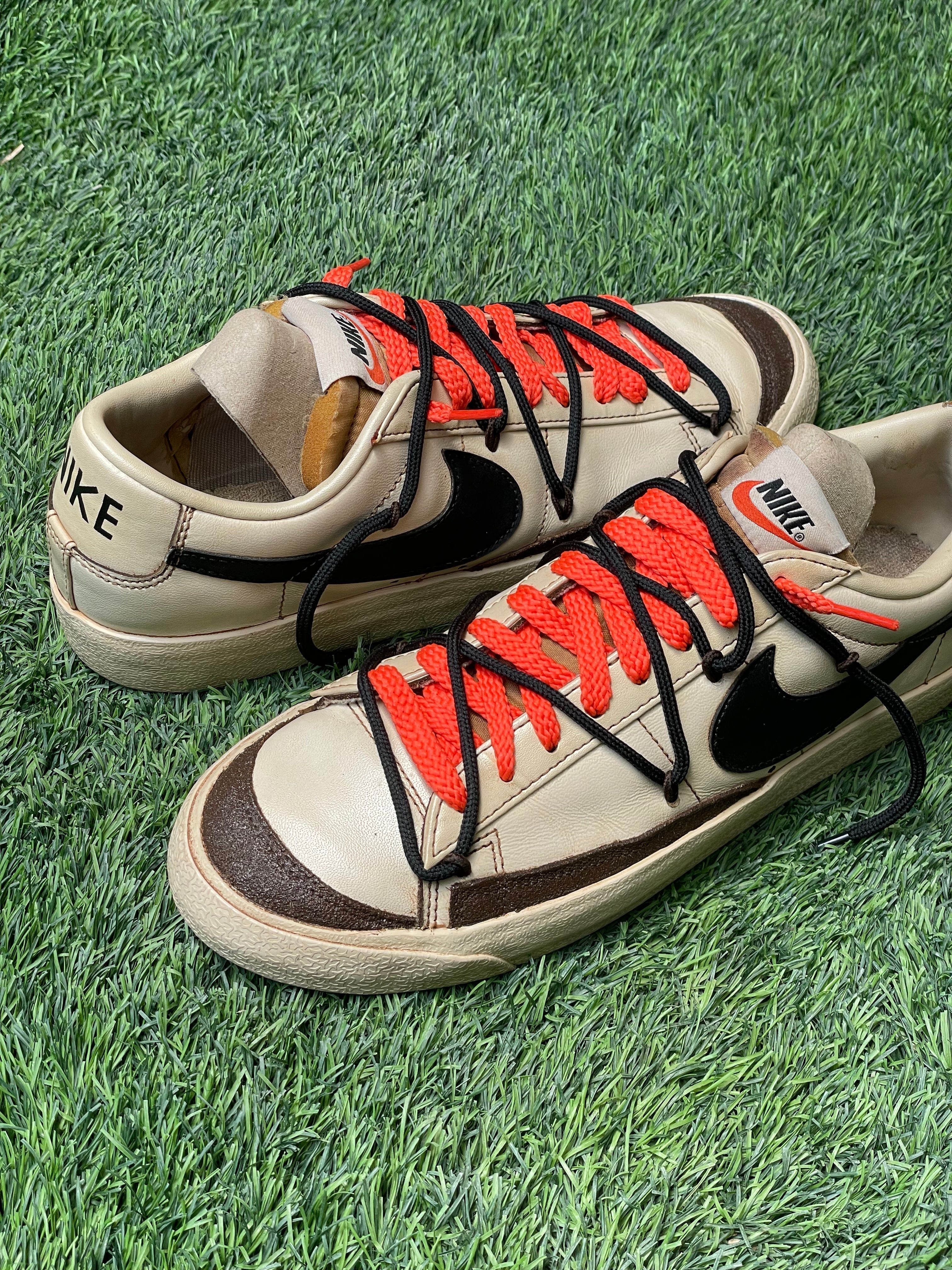 Cream Nike sneakers with black swoosh, red and black laces on grass background