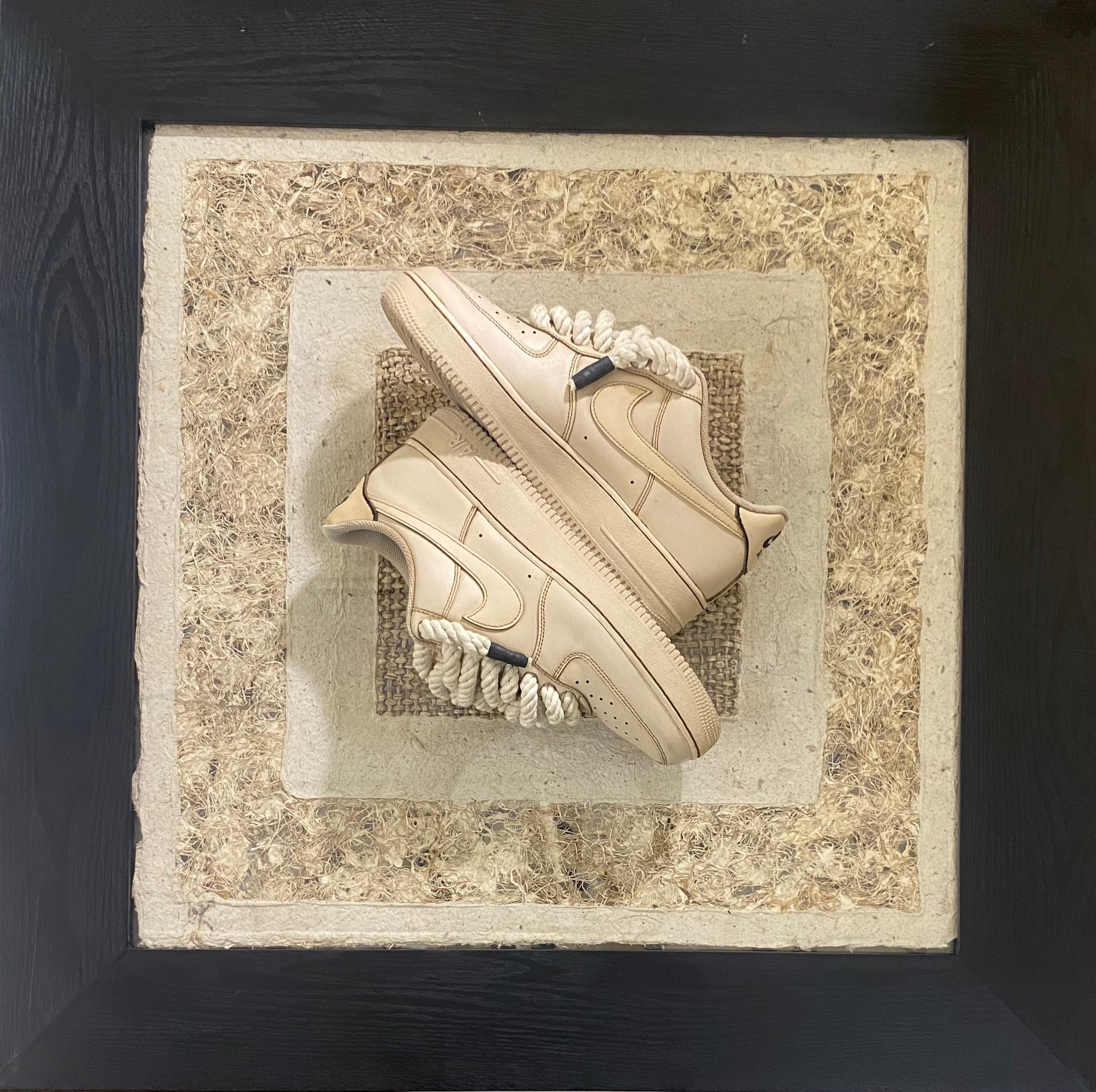 Beige streetwear sneakers with rope laces displayed on textured, layered background