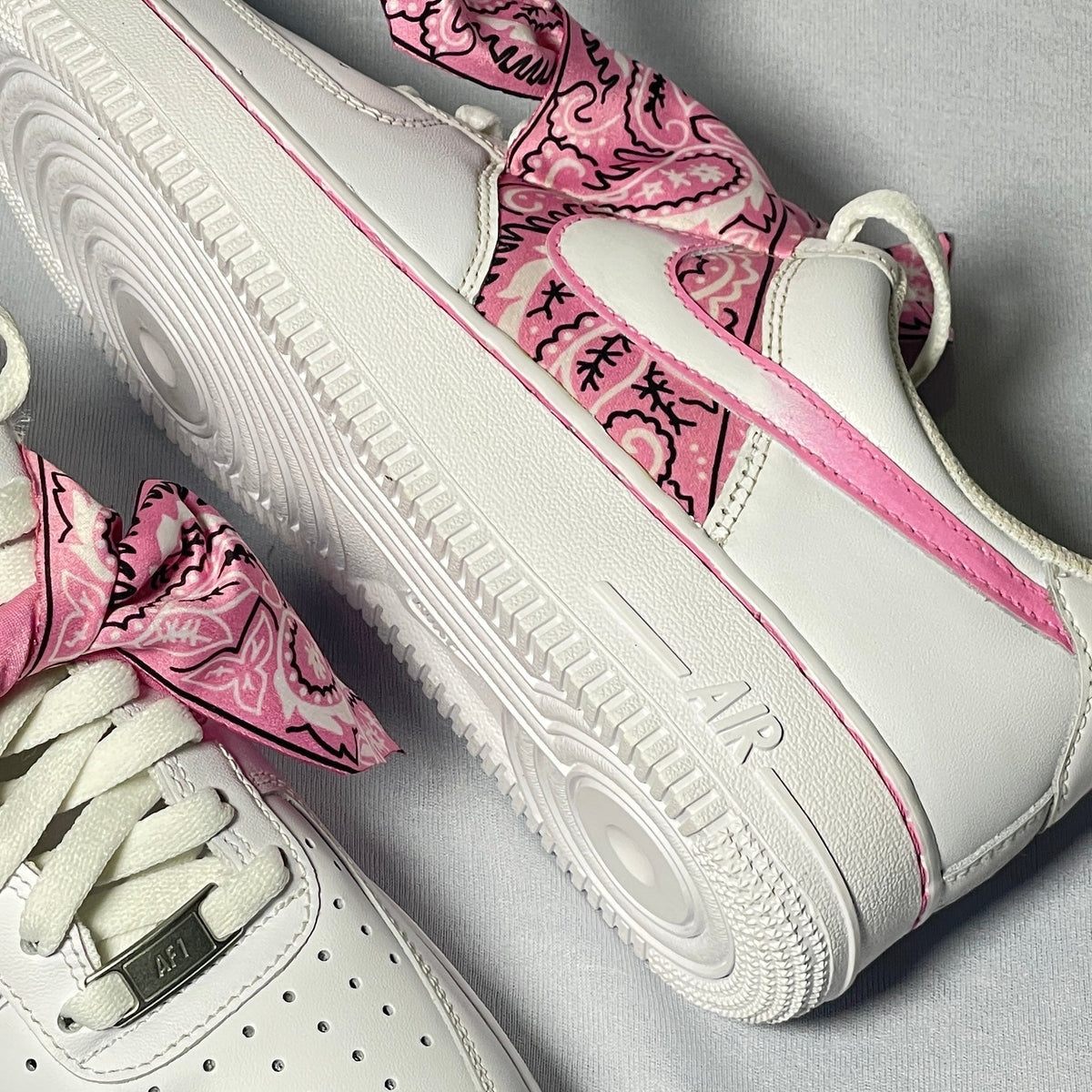 White leather sneakers with pink paisley bandana details and pink accents, streetwear style.
