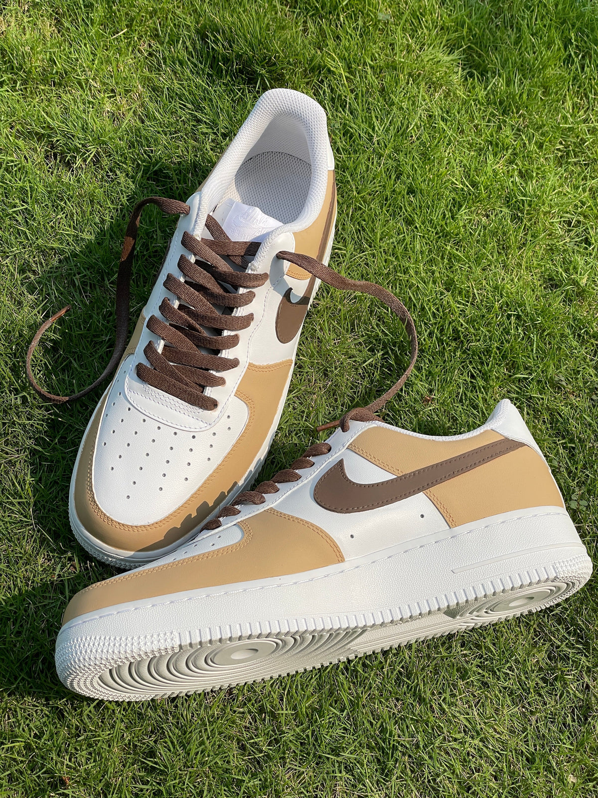 Tan and white Nike sneakers with brown swoosh and laces on green grass