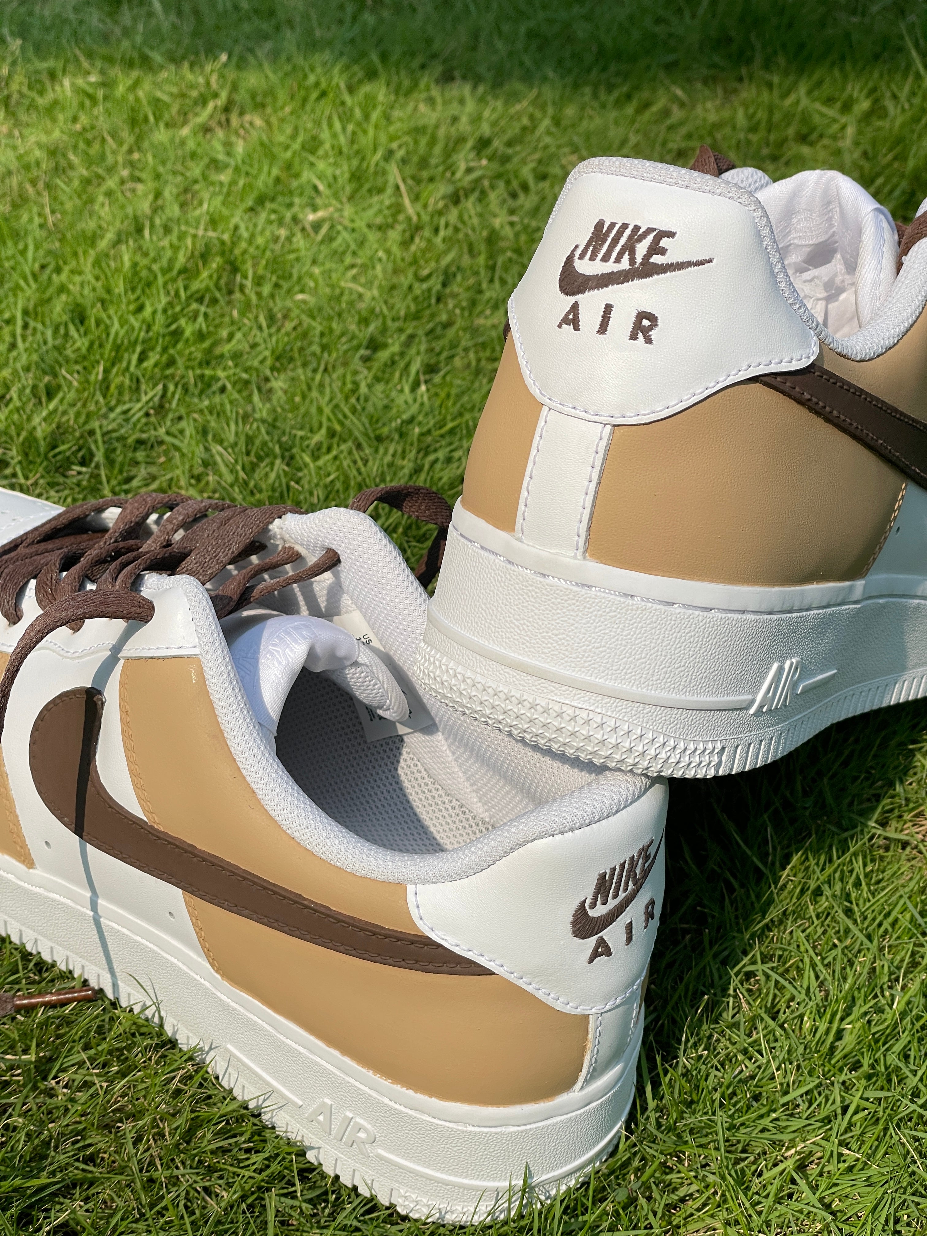 Tan and white Nike Air Force 1 sneakers with brown swoosh on green grass outdoors