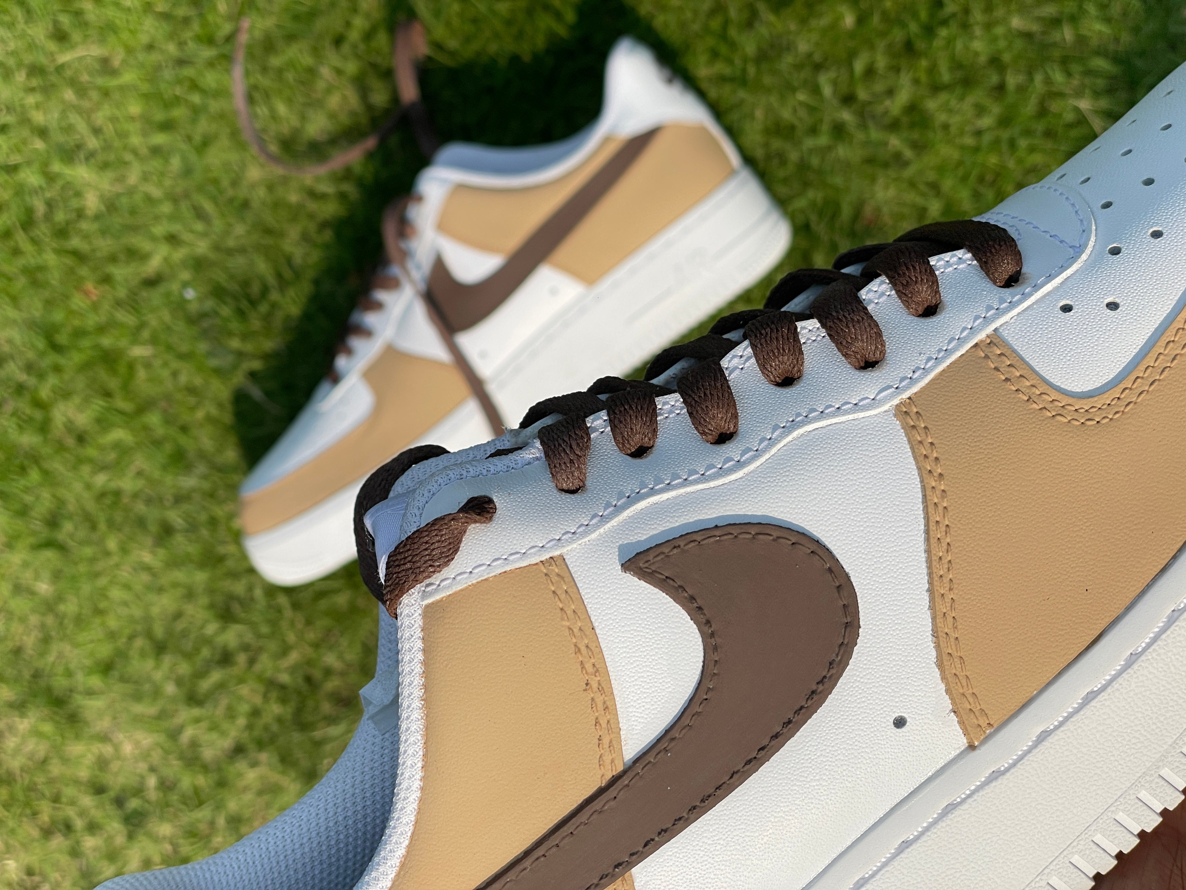 Beige and white leather sneakers with brown swoosh and laces on green grass