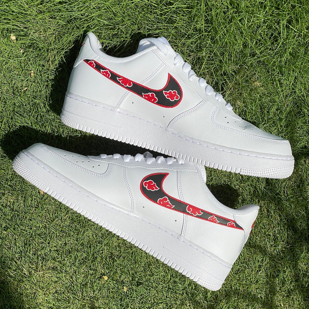 White streetwear sneakers with custom red-black graphic swoosh, displayed on grass outdoors