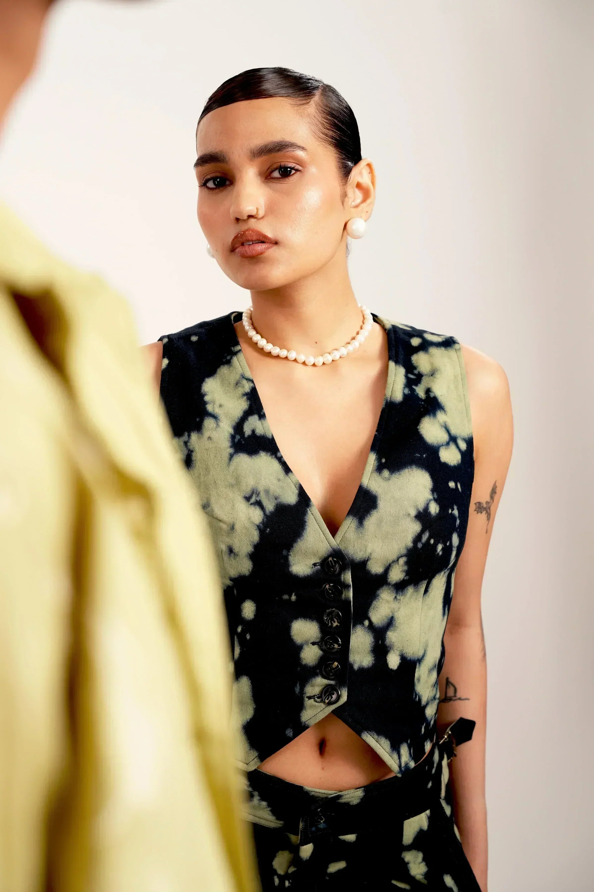 Young woman with sleek hair wearing black and green tie-dye vest and pearl necklace in studio