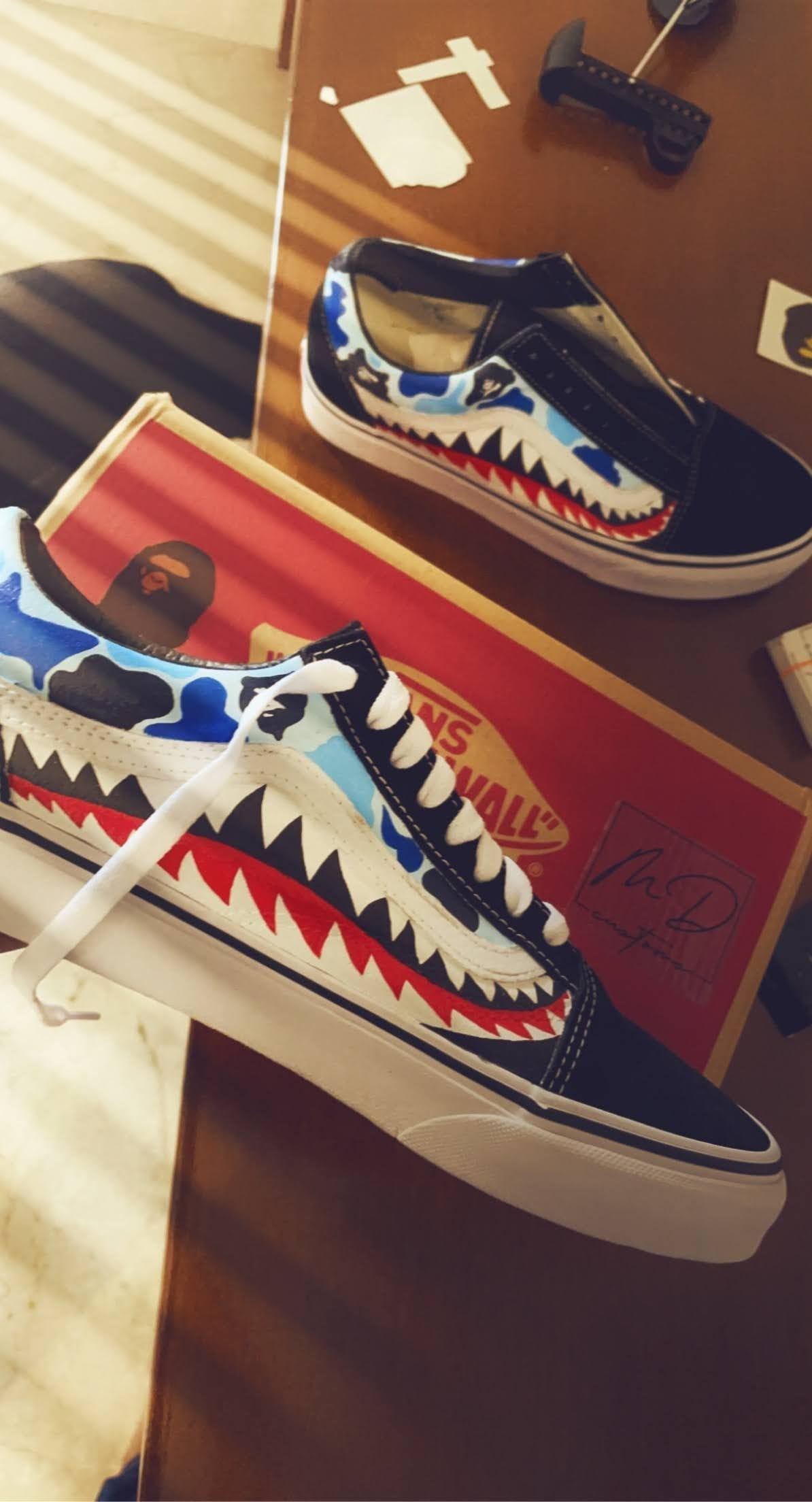 Custom Vans sneakers with blue camo and shark teeth design on a wooden table.