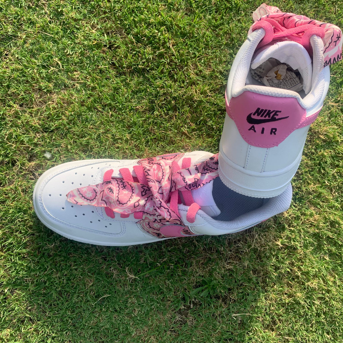 White Nike Air sneaker with pink paisley laces on grass, streetwear footwear style