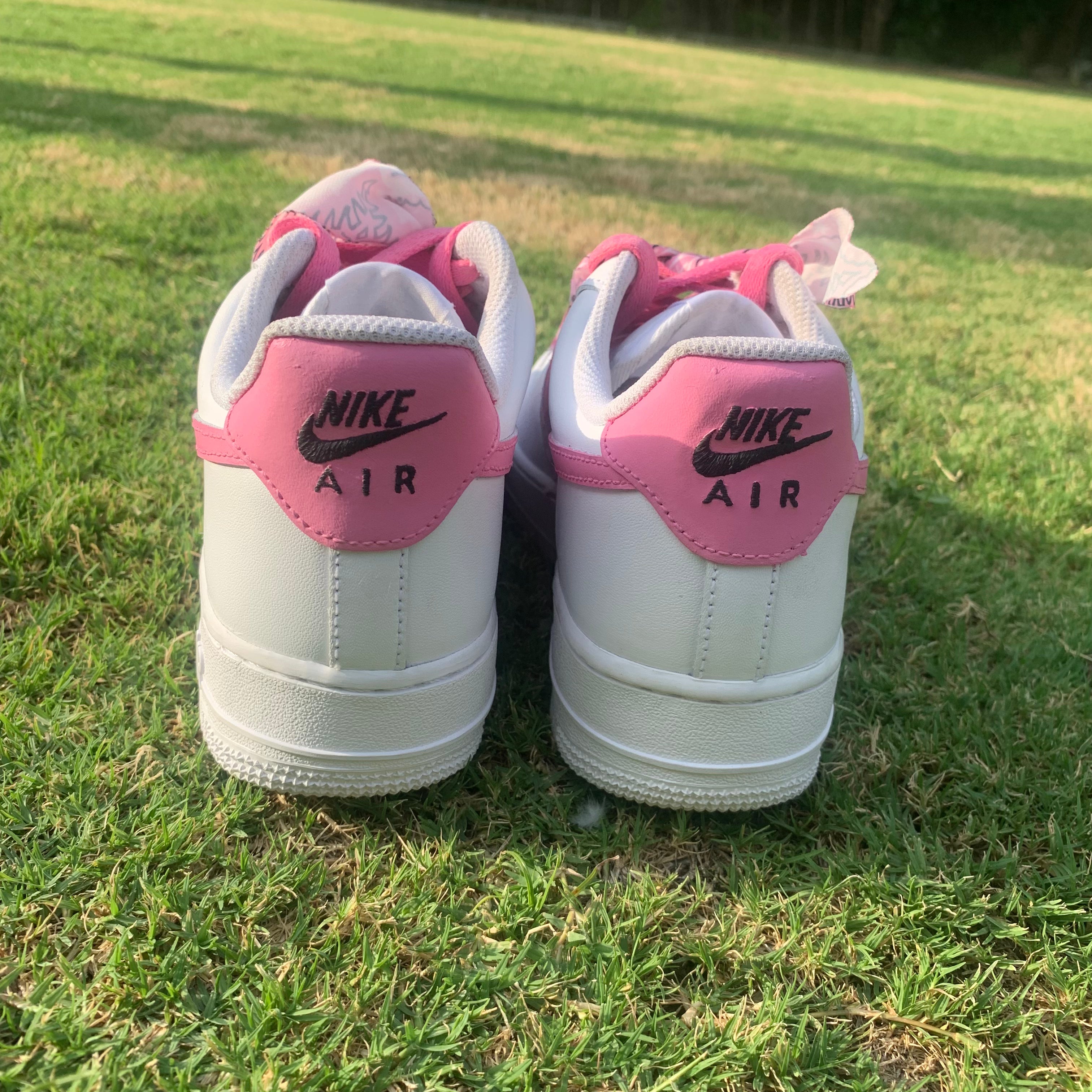 Pair of white and pink Nike Air sneakers on grass, back view, streetwear style footwear