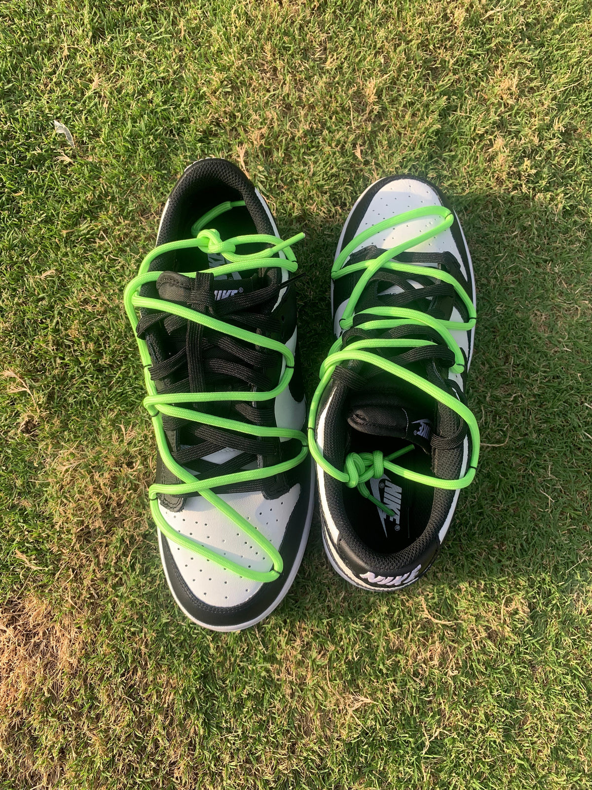 Black and white Nike sneakers with bright green laces on grass, limited edition streetwear shoes