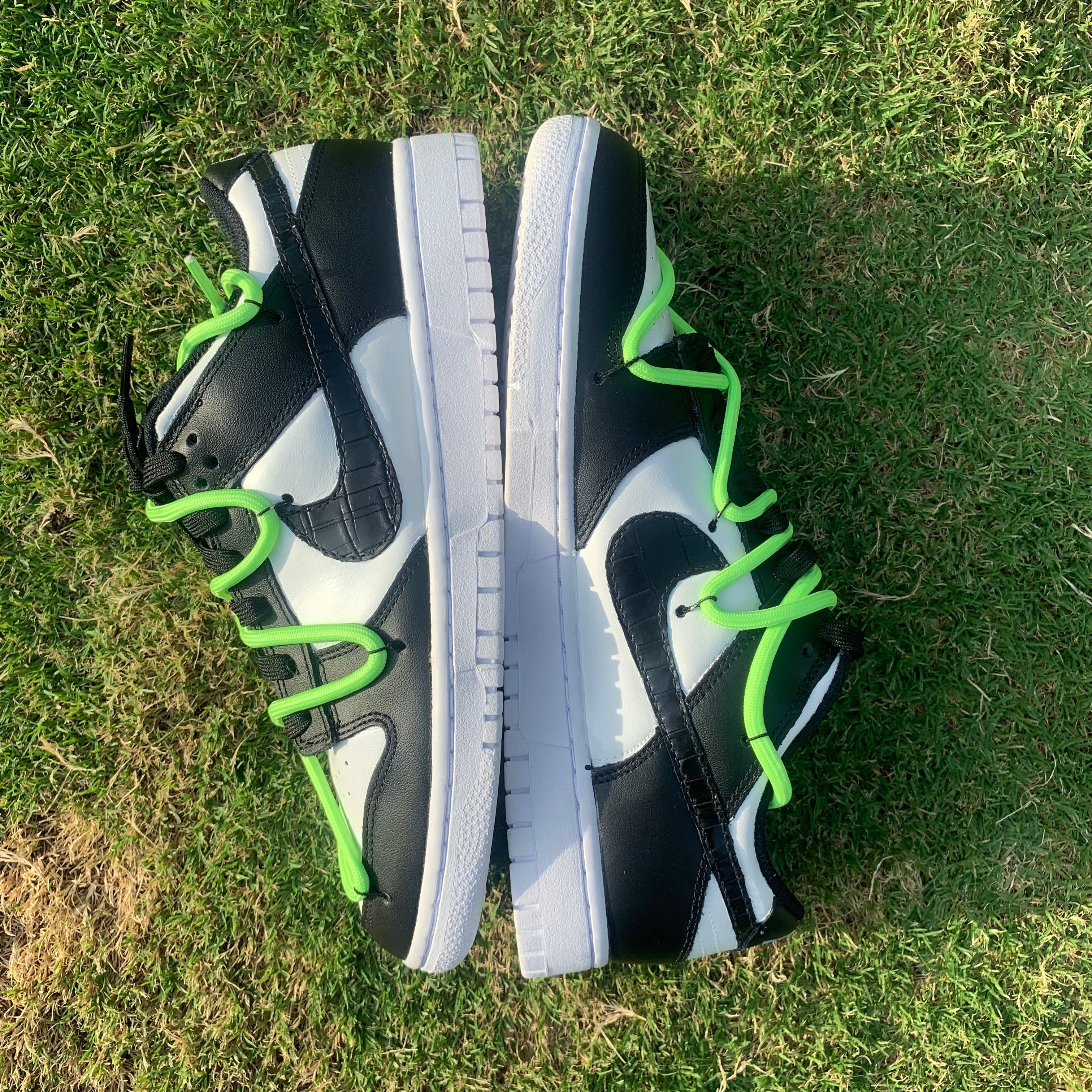 Black and white low-top sneakers with neon green laces on grass, stylish streetwear shoes