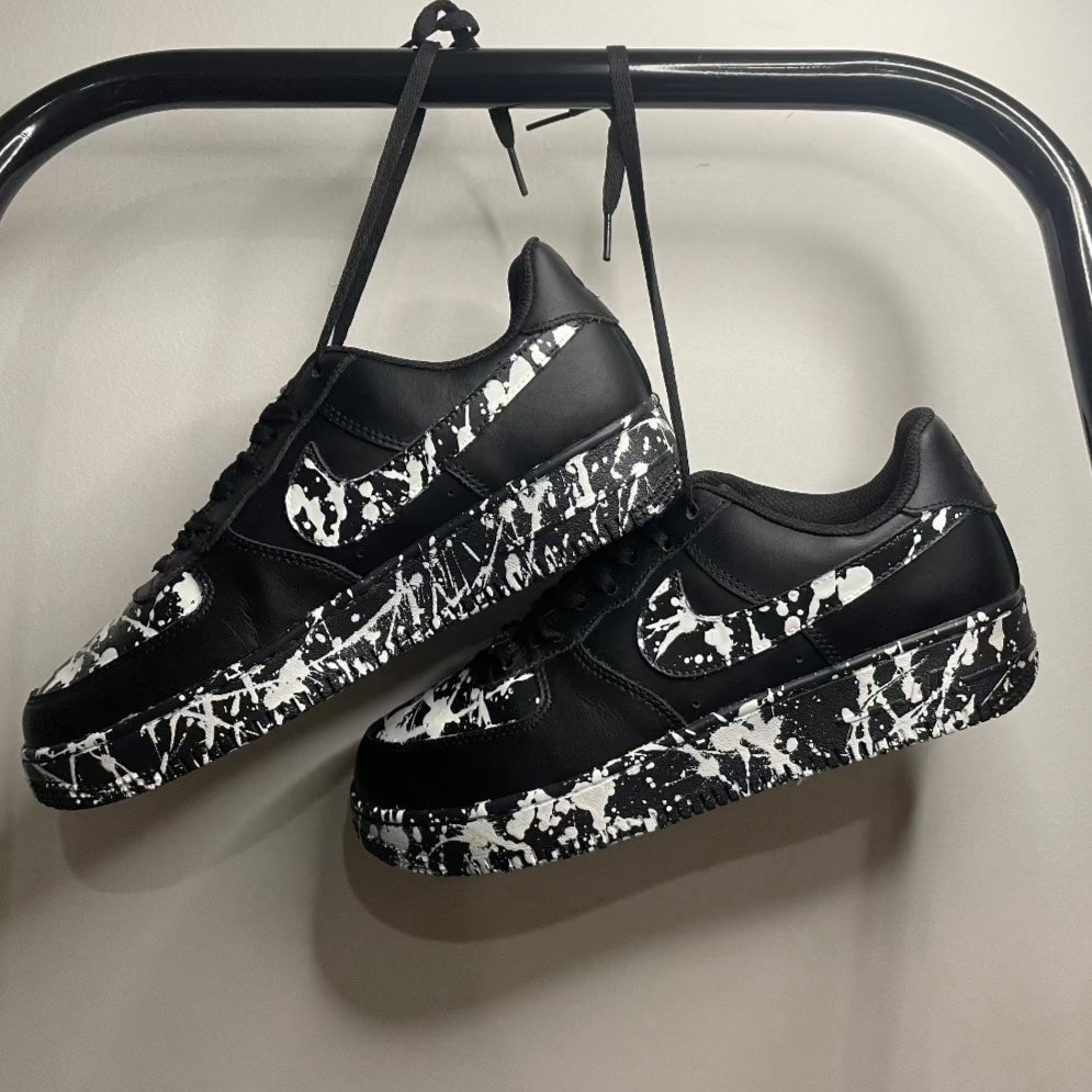 Black streetwear sneakers with white paint splatter design hanging on a clothing rack