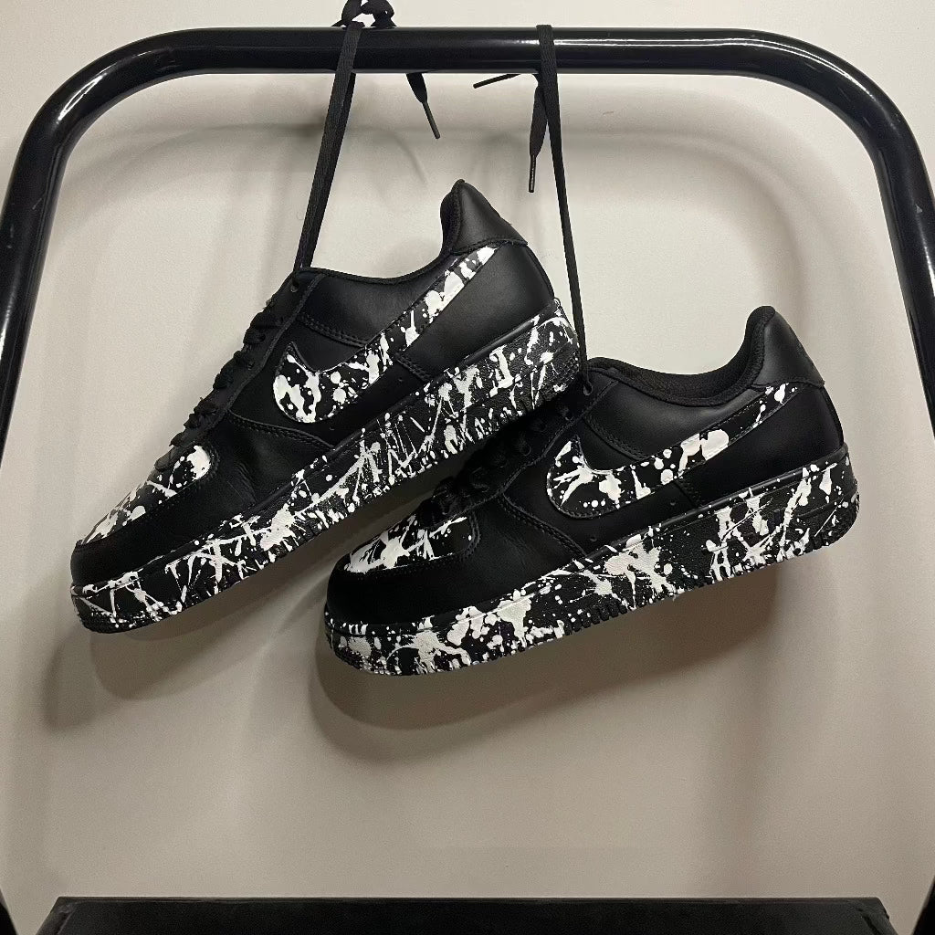 Black streetwear sneakers with white paint splatter design hanging on a rack