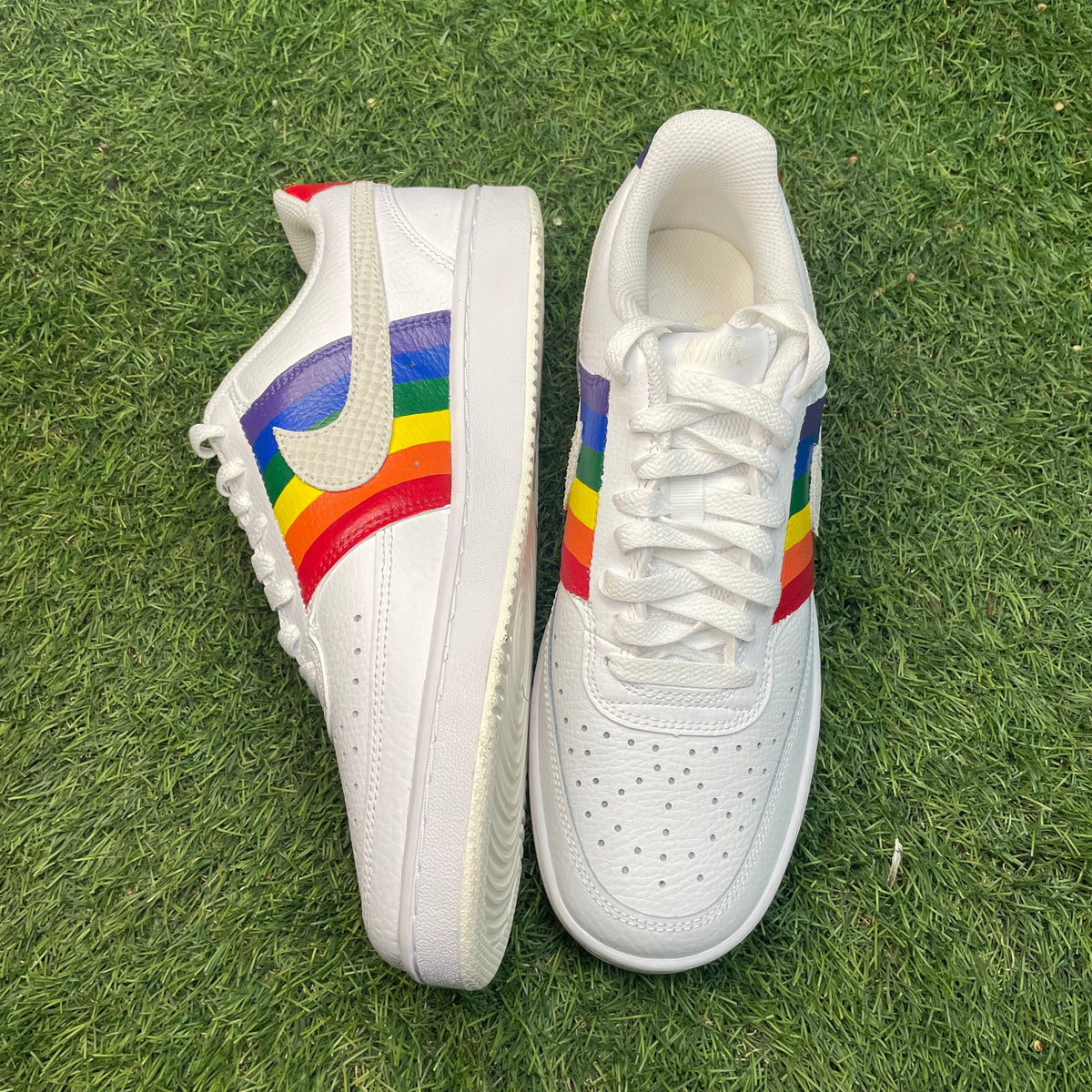 White leather sneakers with rainbow accents on side, displayed on grass