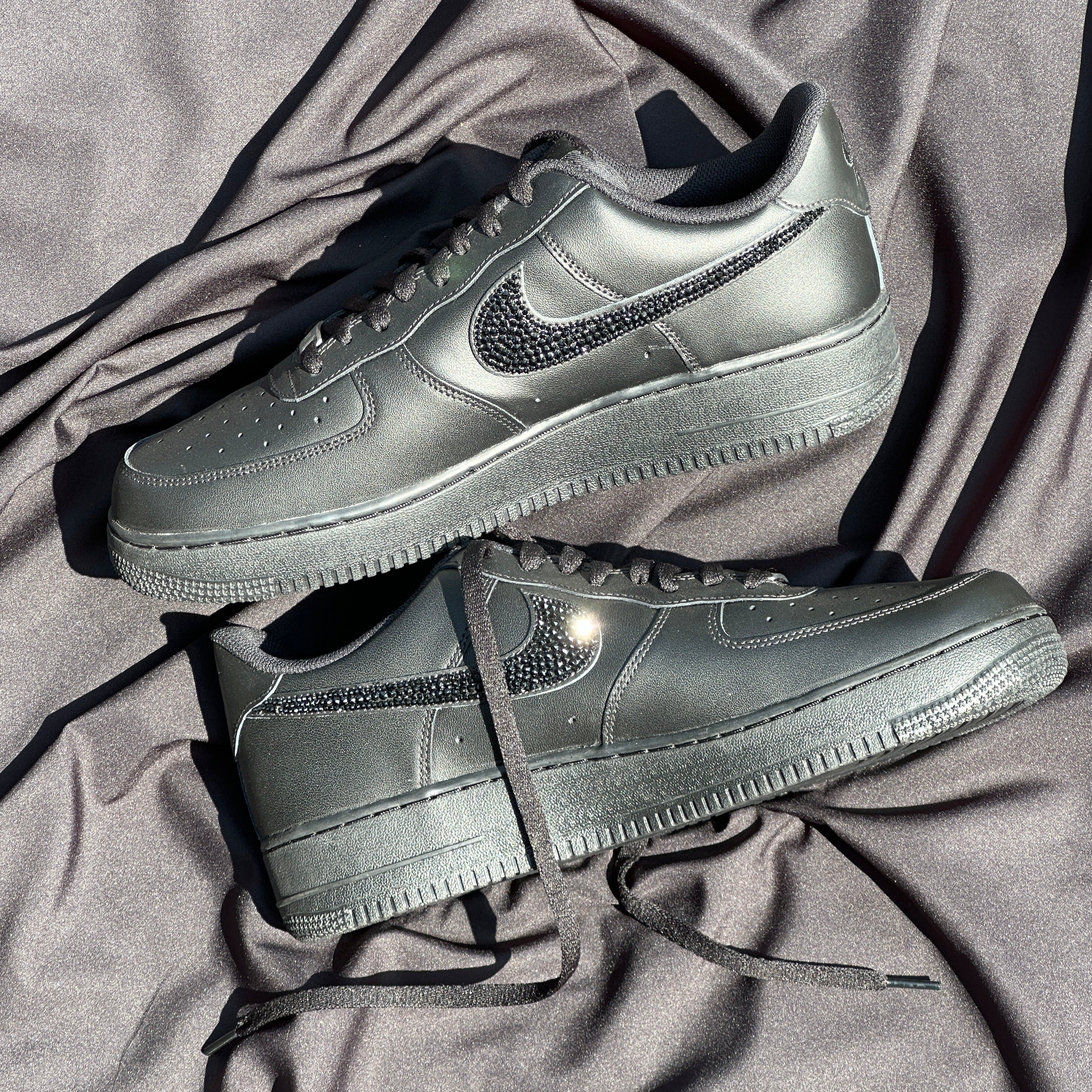 Black leather streetwear sneakers with crystal-embellished swoosh on a satin backdrop