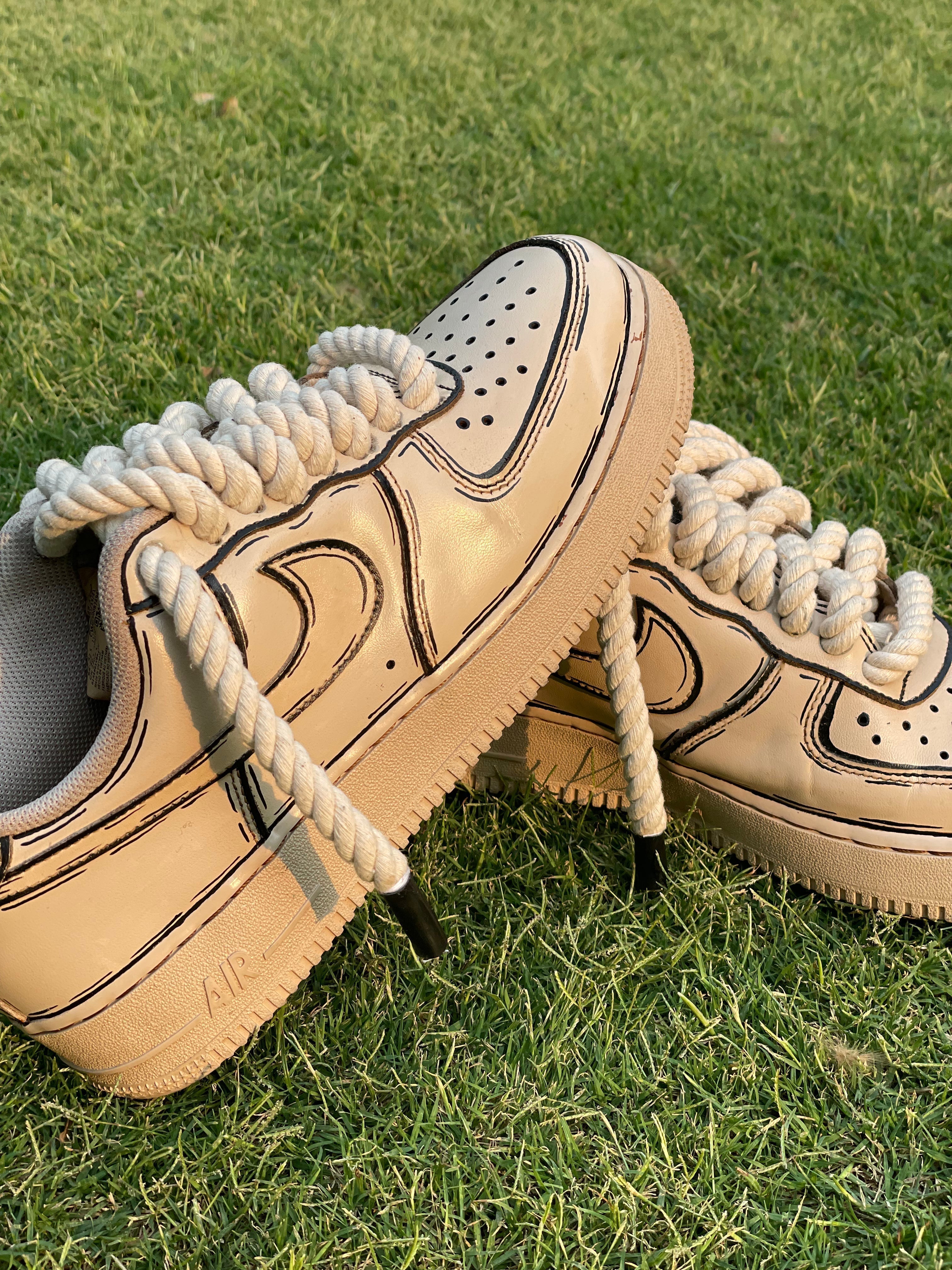 Beige streetwear sneakers with thick rope laces and black outline details on grass