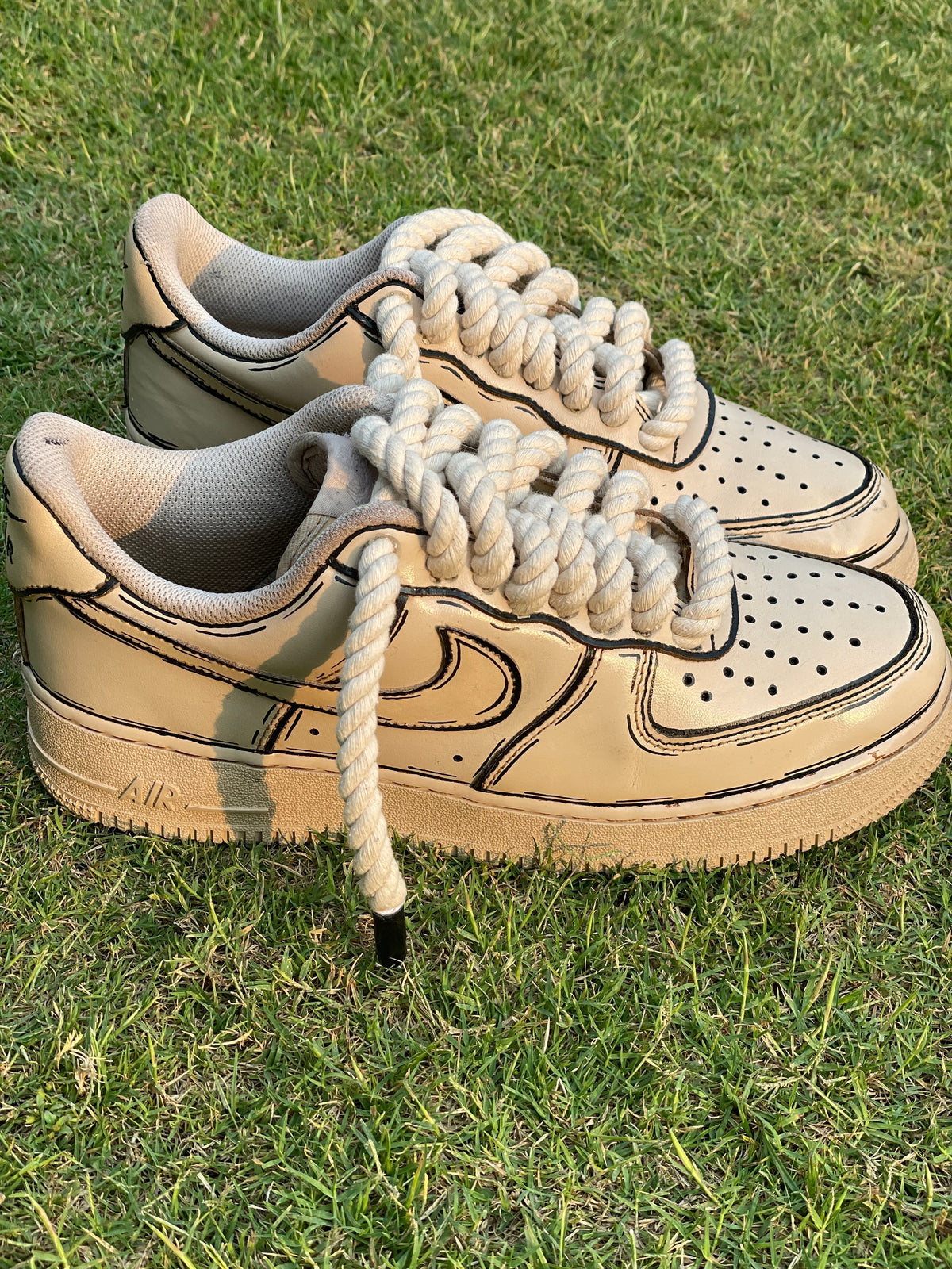 Beige streetwear sneakers with thick rope laces and black outline design on grass