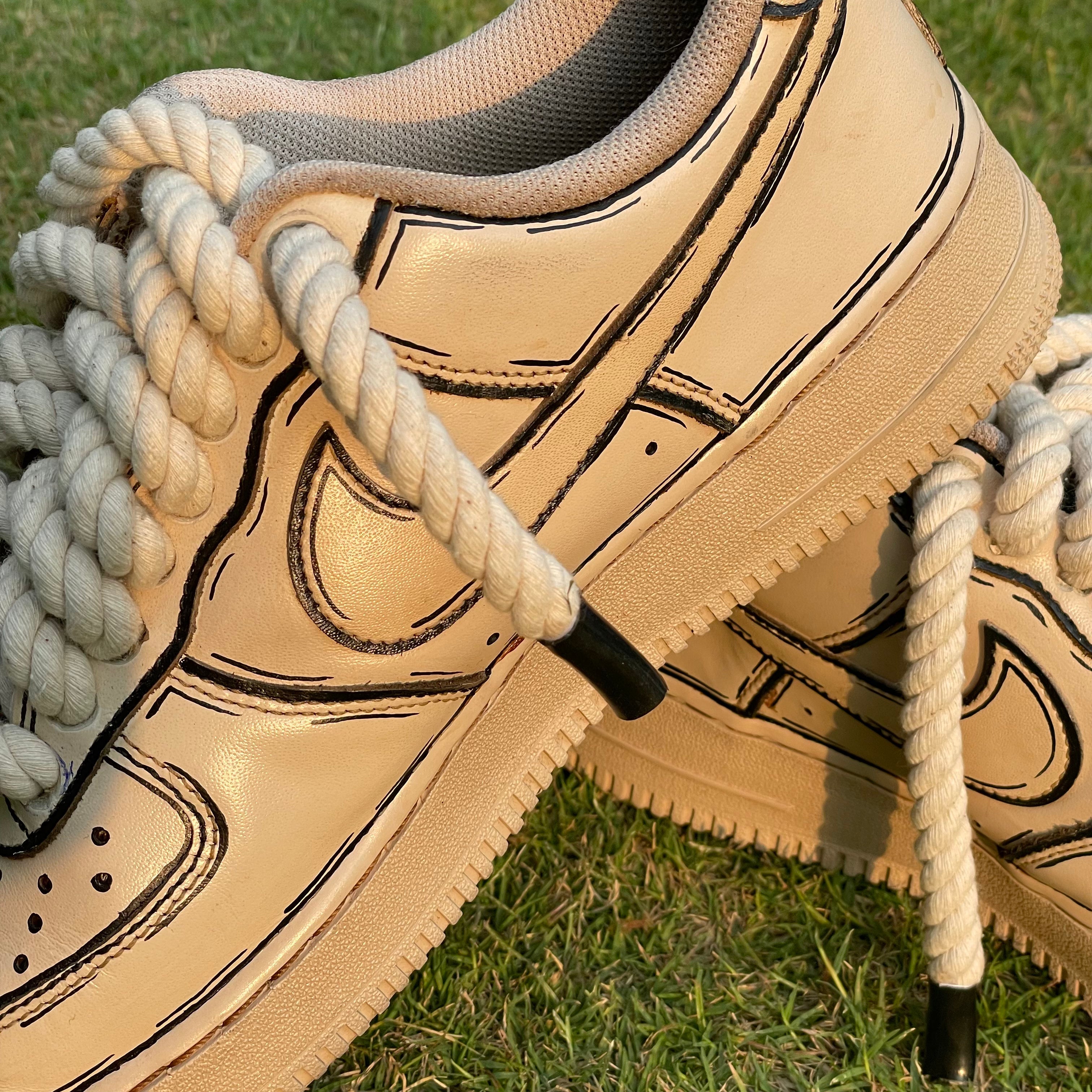 Beige streetwear sneakers with thick rope laces and bold black stitching on grass