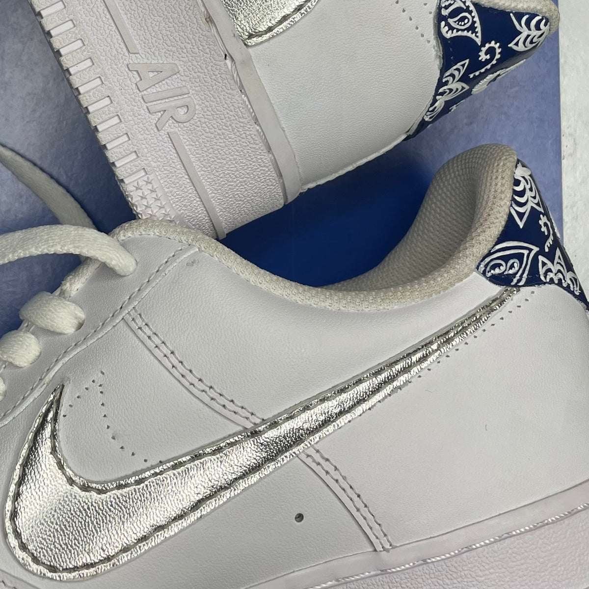 White sneakers with silver swoosh and blue paisley heel detail, streetwear style