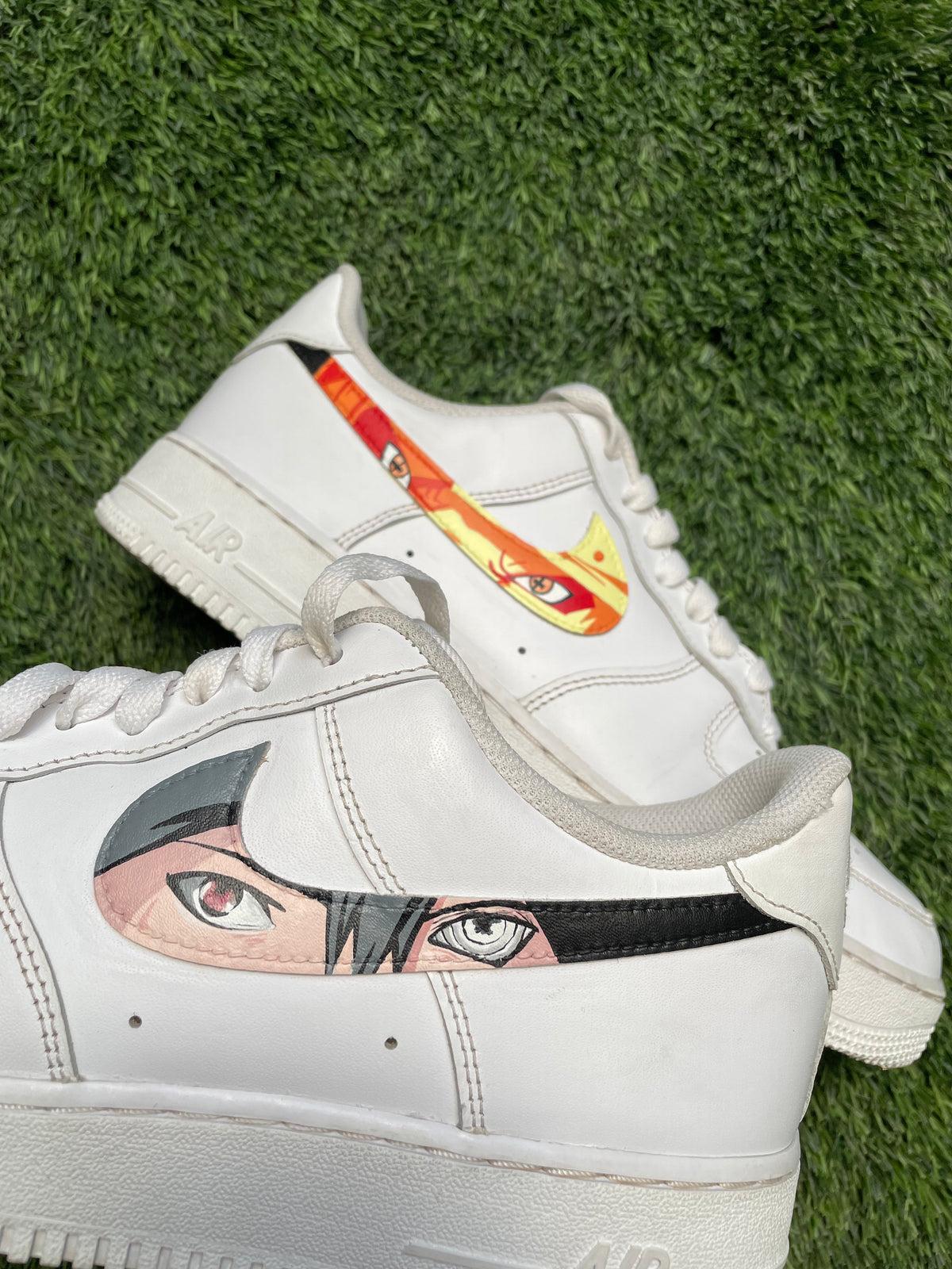 Custom white sneakers with anime eye art on swoosh, displayed on green grass