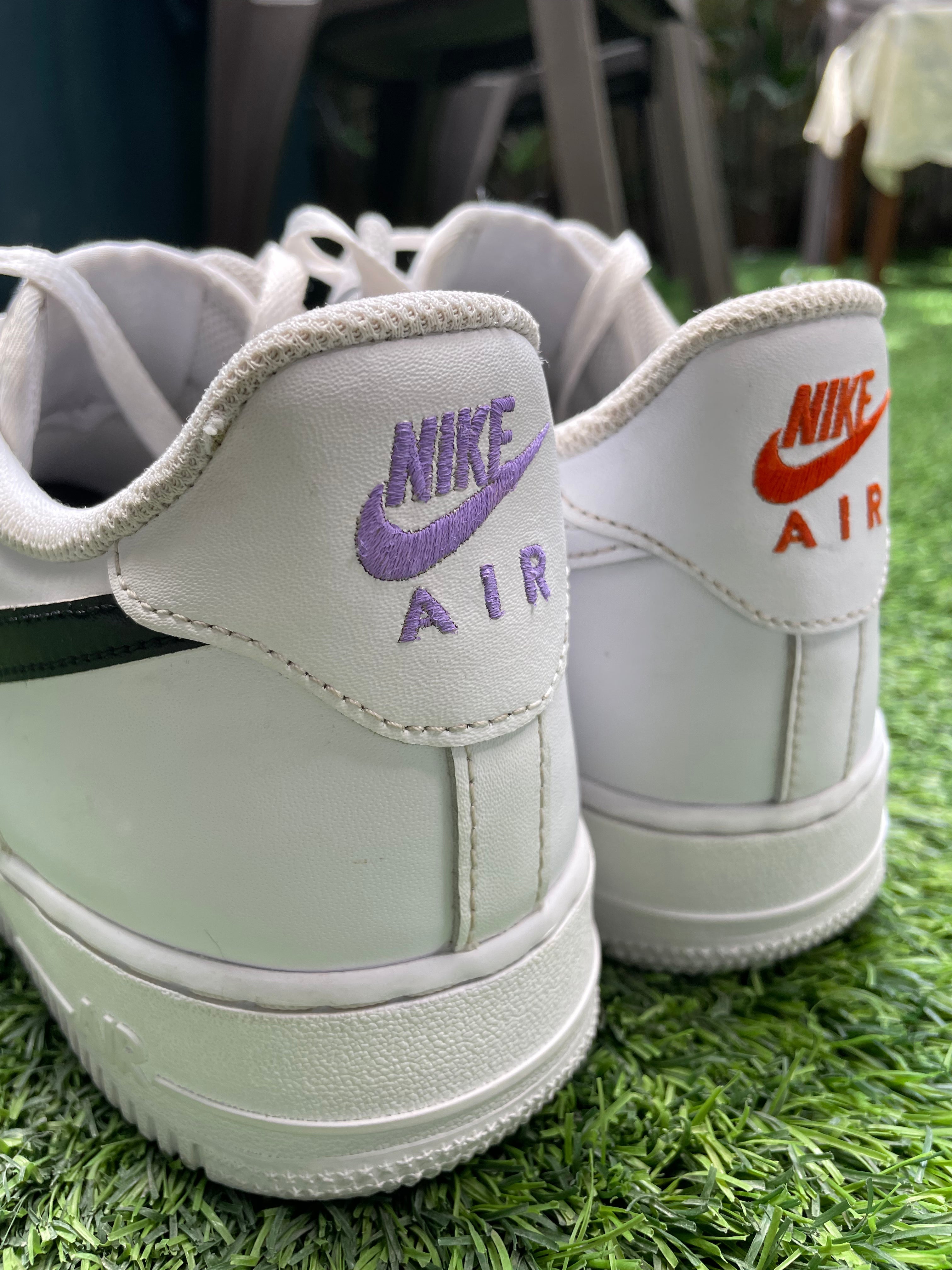 White Nike Air sneakers with purple and orange stitched logos, outdoor on grass