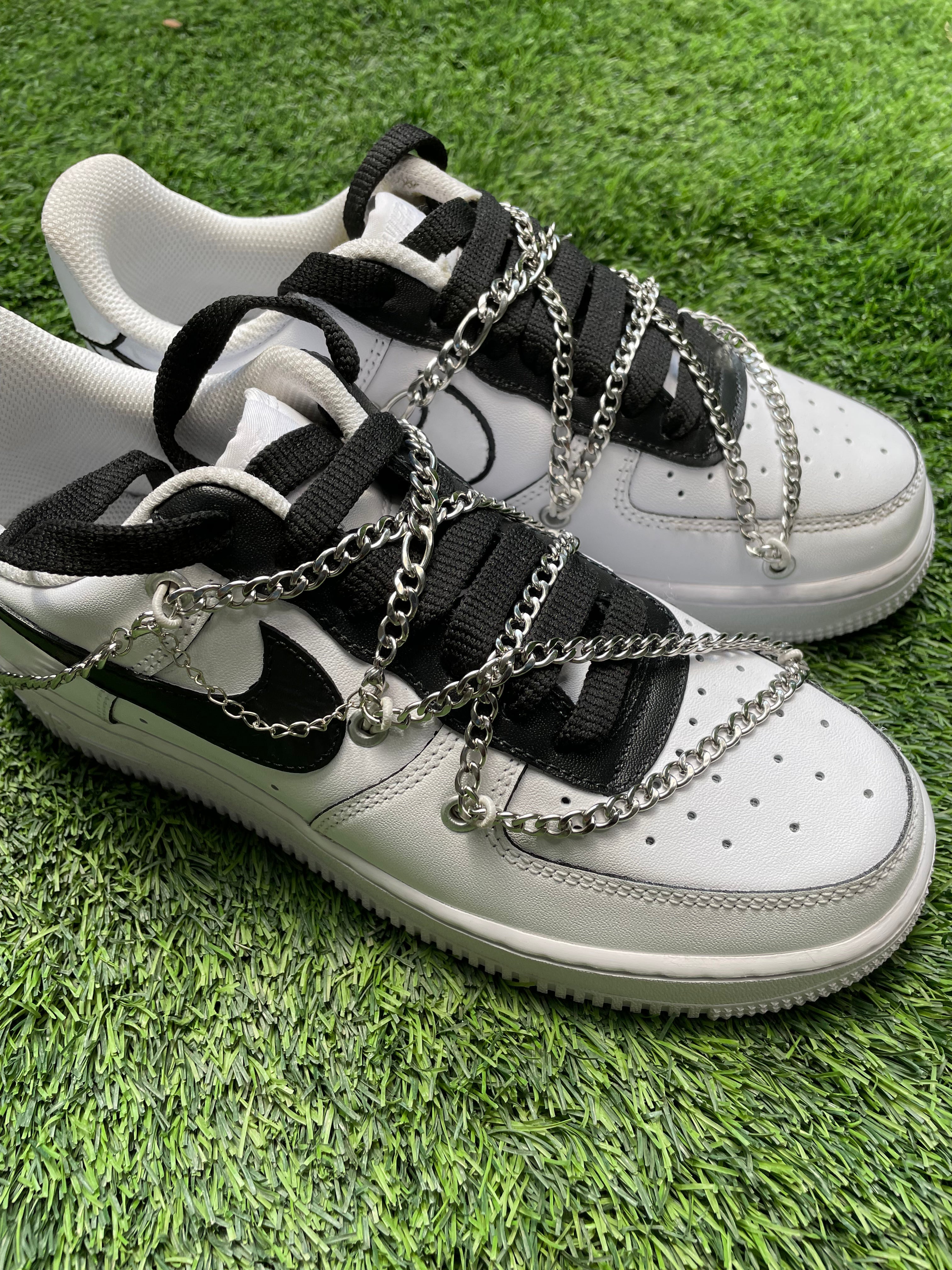 White and black streetwear sneakers with chunky chain accents on grass