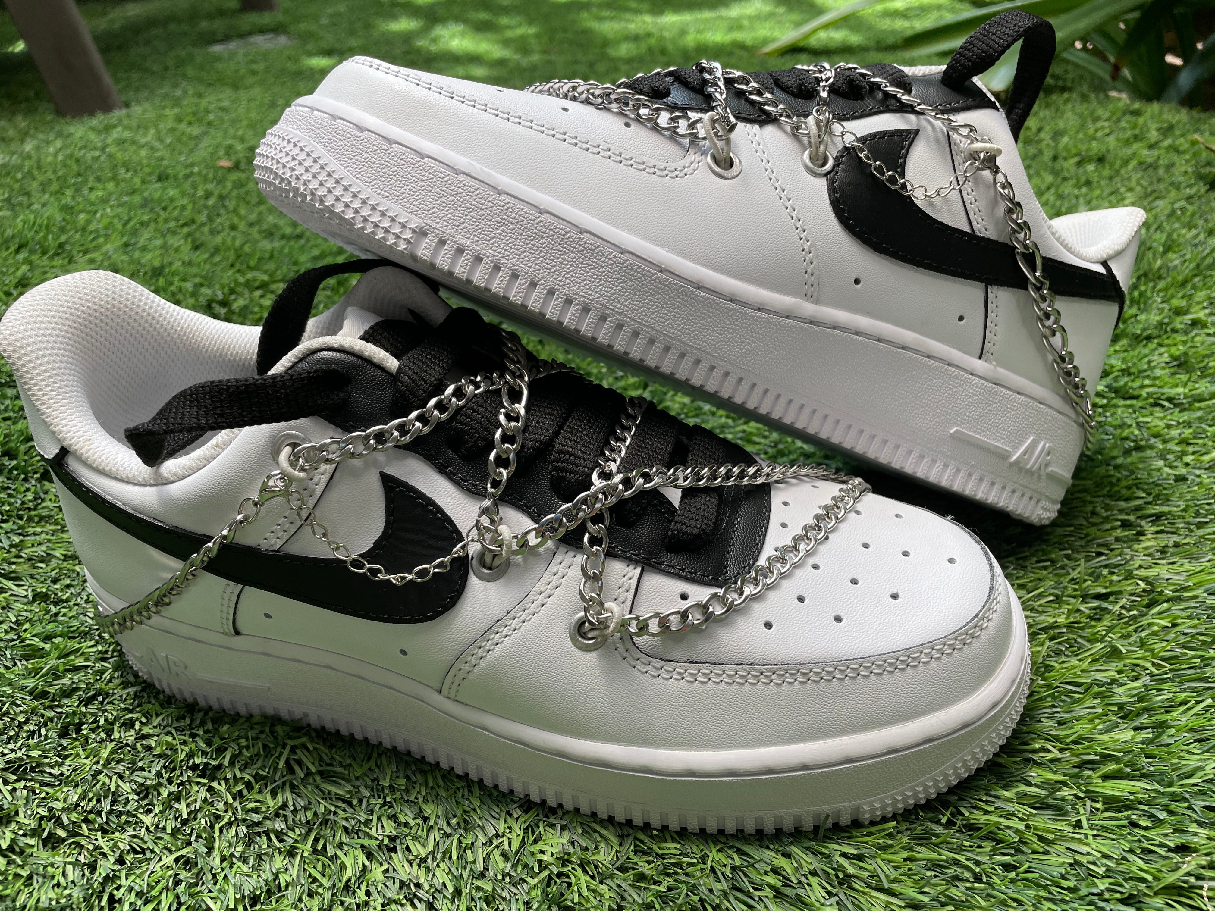 White and black streetwear sneakers with silver chains, displayed on green grass.