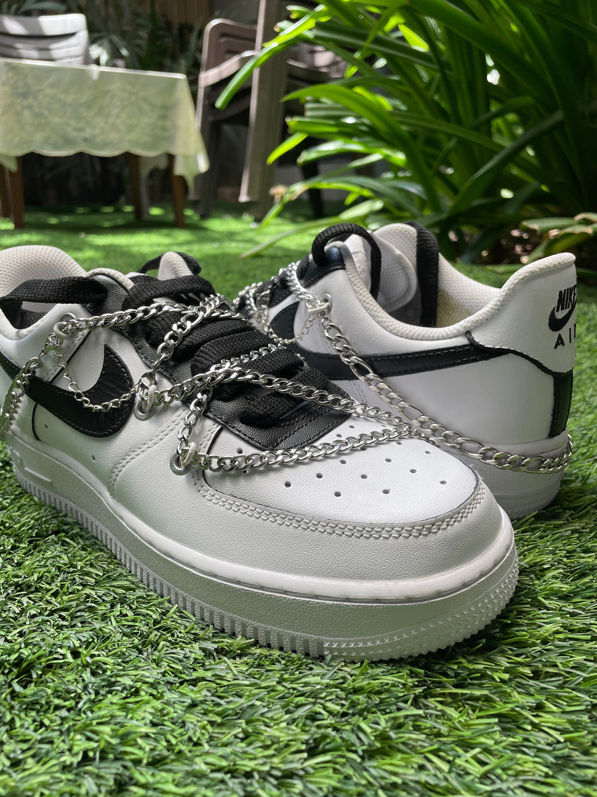 Black and white Nike Air Force 1 sneakers with silver chains on artificial grass outdoors