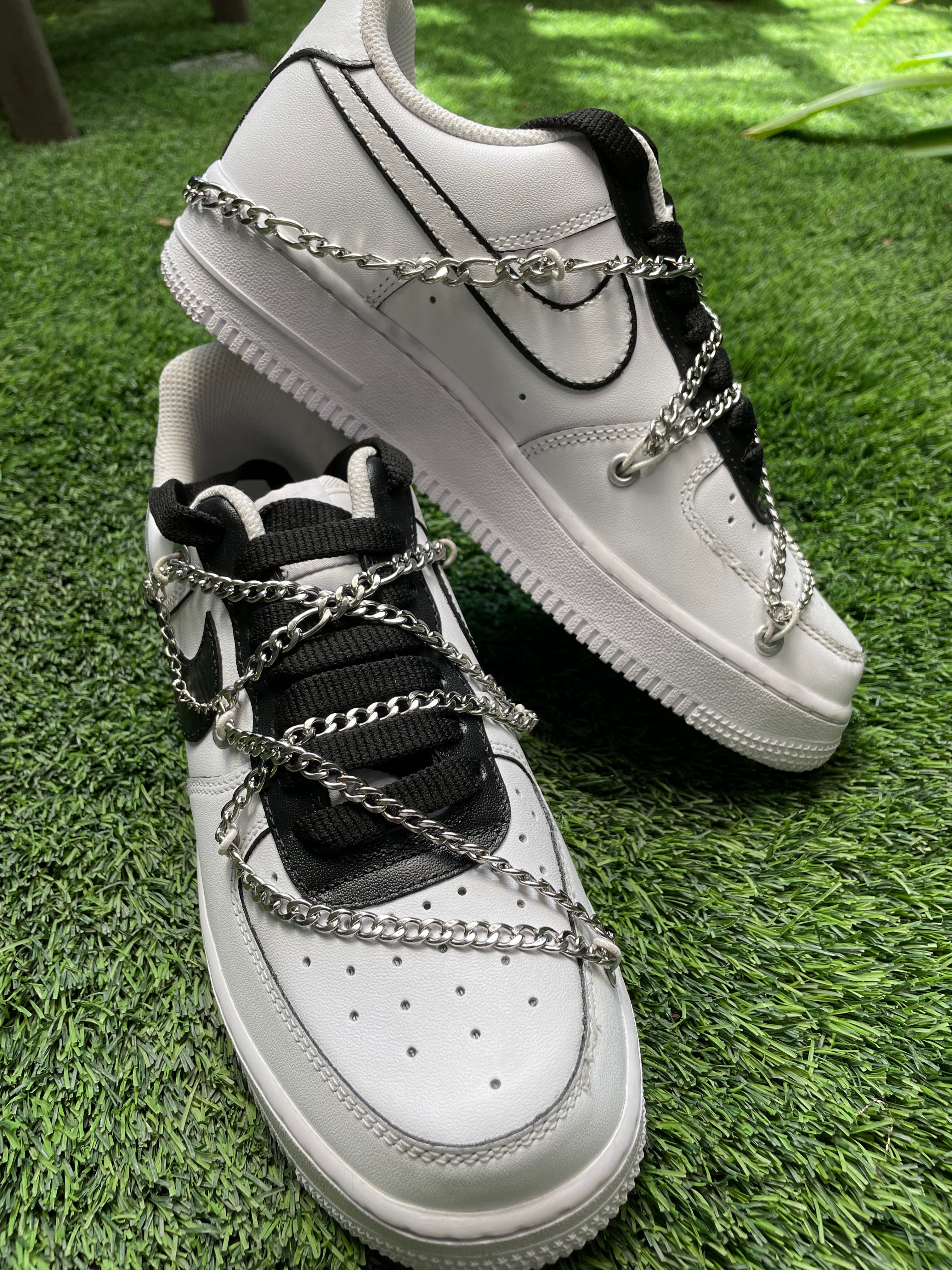 White low-top sneakers with silver chain accents and black details on green grass