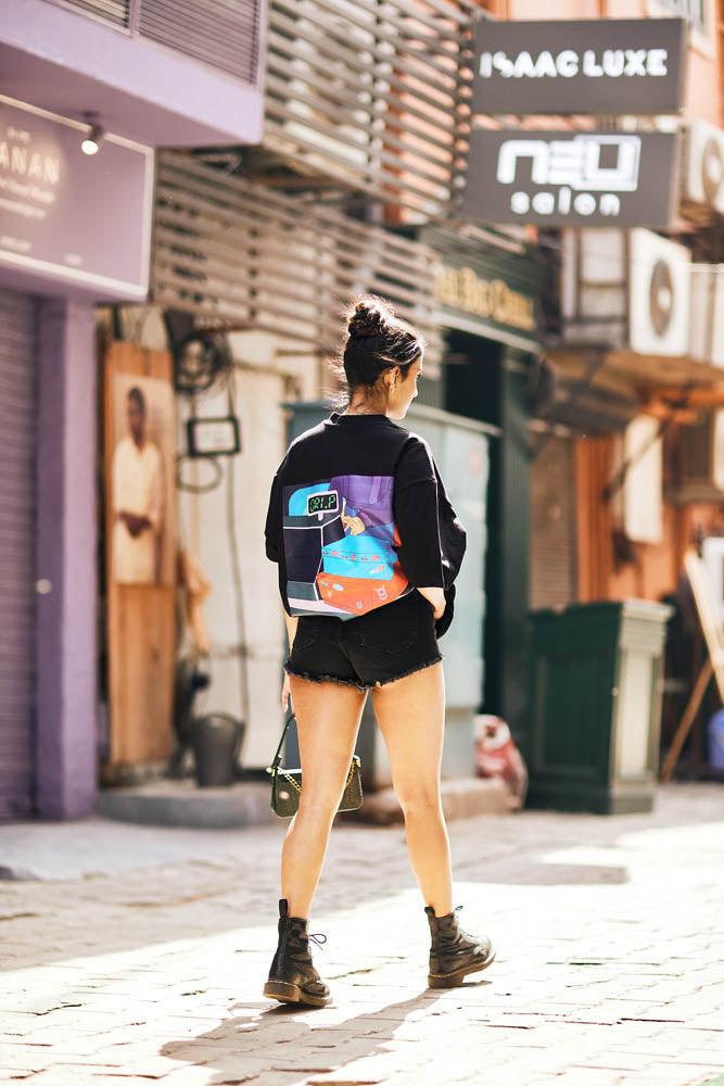 Woman in streetwear jacket, black shorts, combat boots, walking on an urban street.