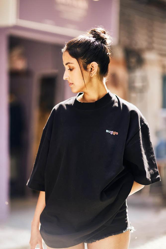 Woman wearing oversized black streetwear t-shirt with 'sugga' logo, urban background