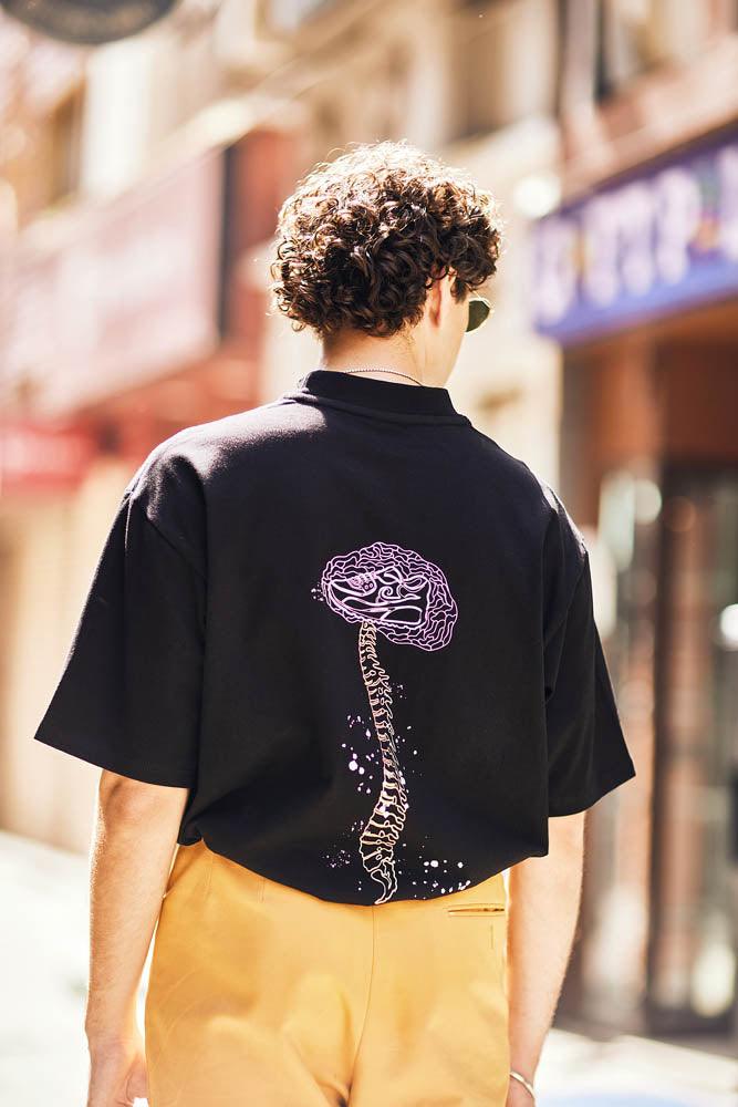 Man wearing black streetwear t-shirt with purple brain and spine graphic, city background